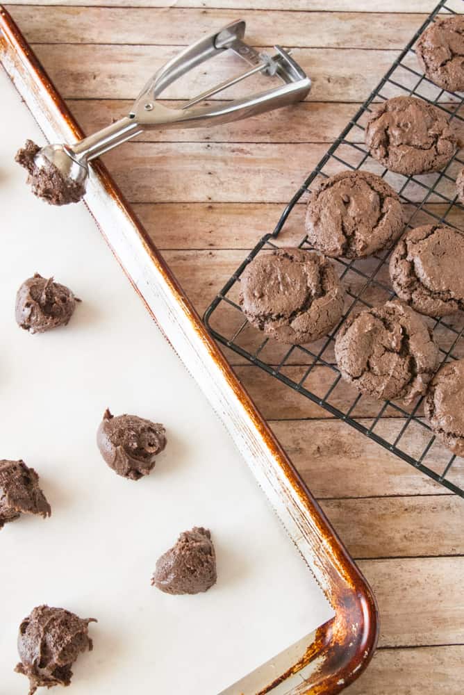 Chocolate cookies scooped onto a baking sheet sitting next to baked ones.