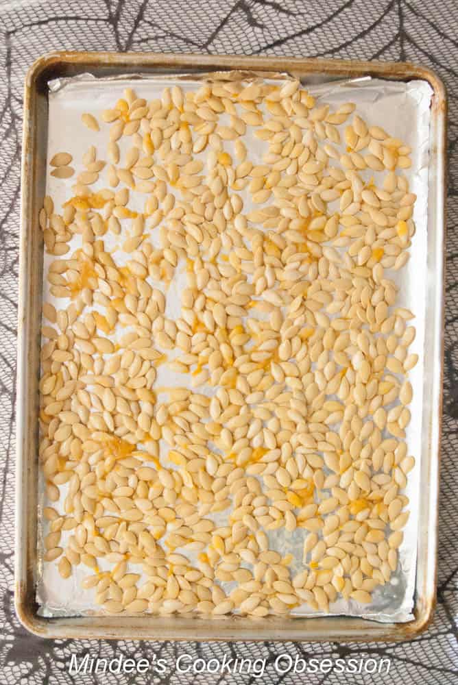Unwashed pumpkin seeds spread across a baking sheet.