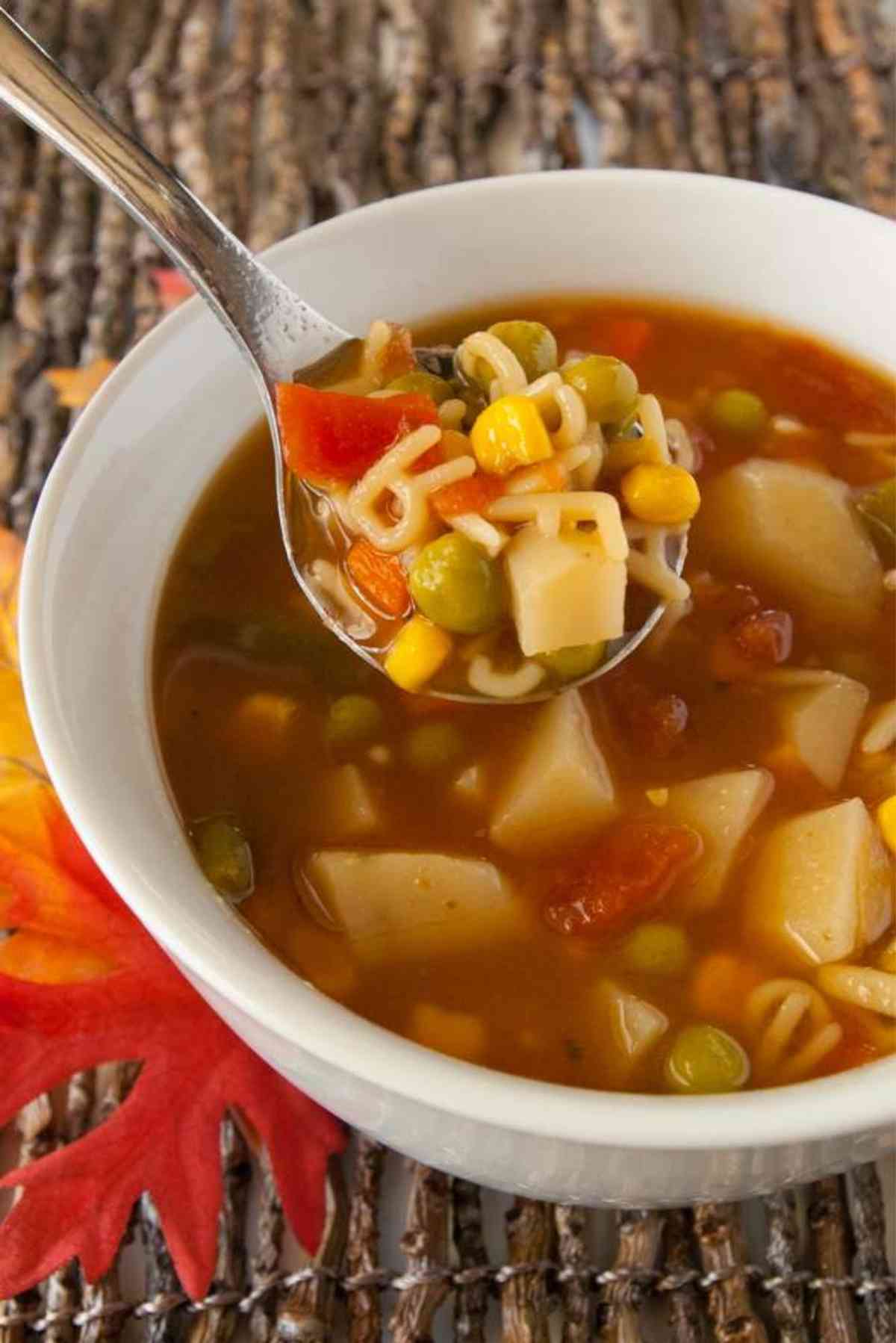 Spoon lifting a bite of alphabet soup from a bowl.