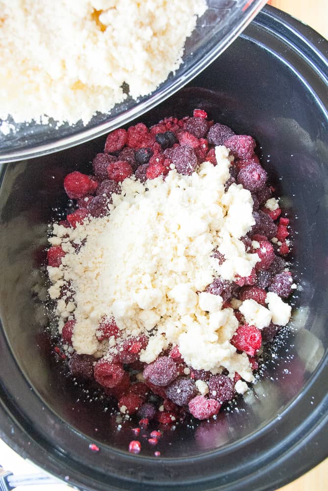 Crumbly cobbler mix being sprinkled over the berries.
