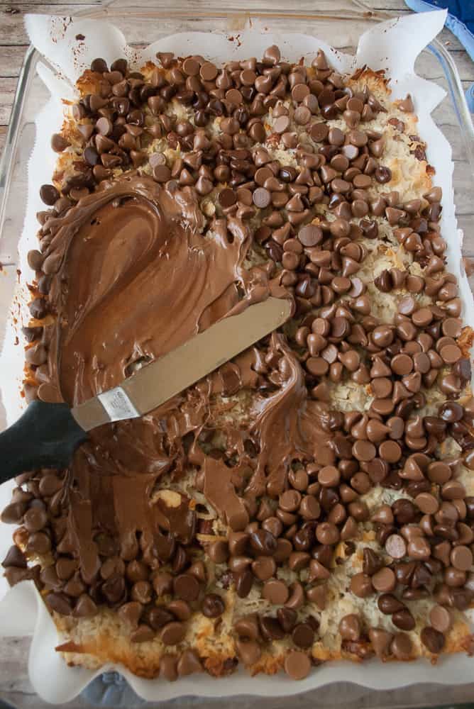 Melted chocolate chips being spread across the top of the almond coconut macaroon bars.
