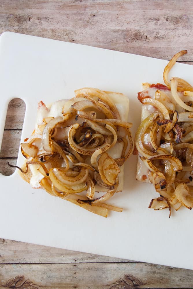 Sourdough halves topped with bacon, a slice of swiss melted and a pile of caramelized onions.