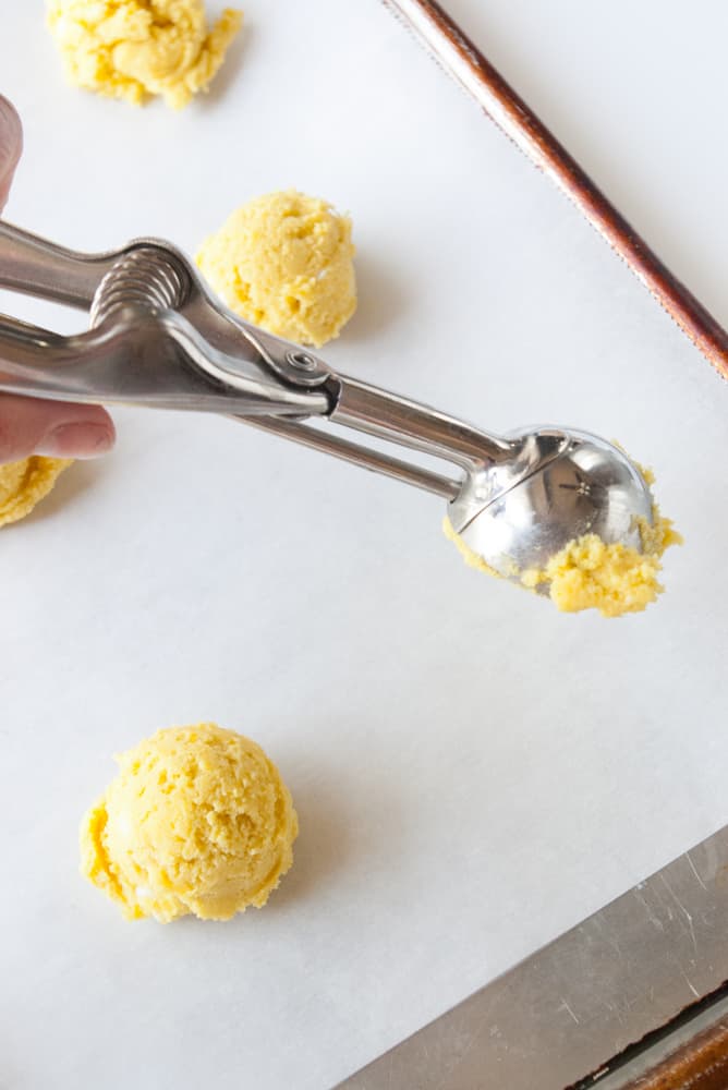 White chocolate Chip lemon cookie dough being scooped out onto a prepared baking sheet.