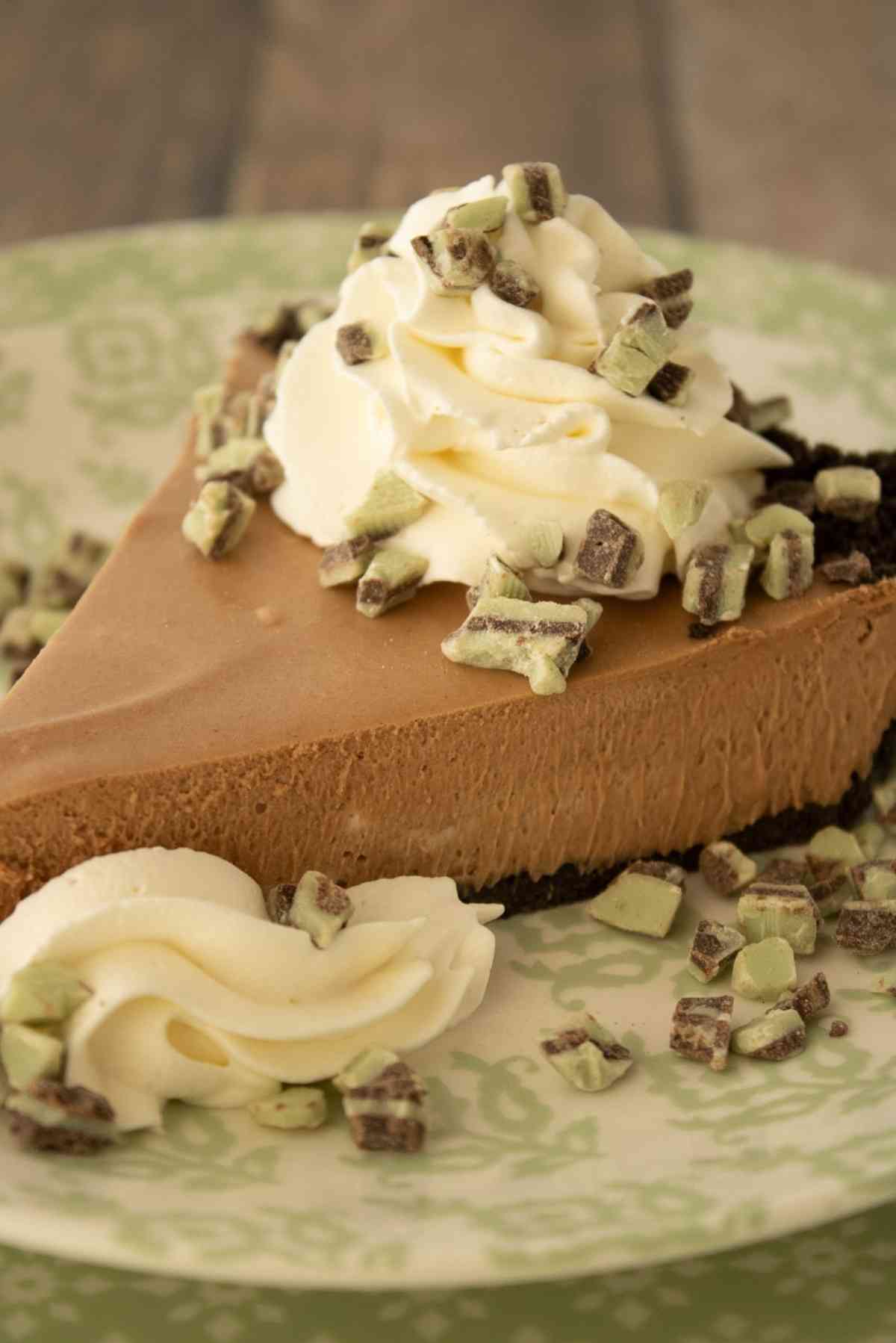 Slice of this chocolate mint grasshopper pie garnished with whipped cream and andes mints.