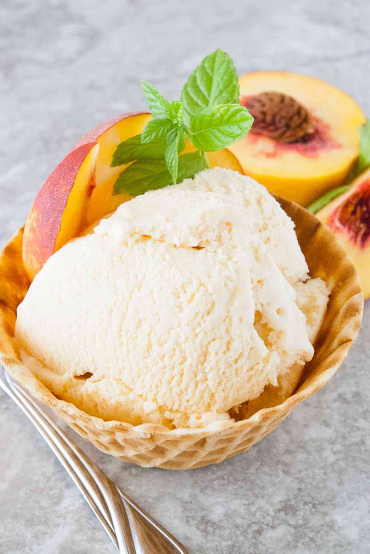 Waffle bowl of homemade peach ice cream garnished with fresh peaches and mint.