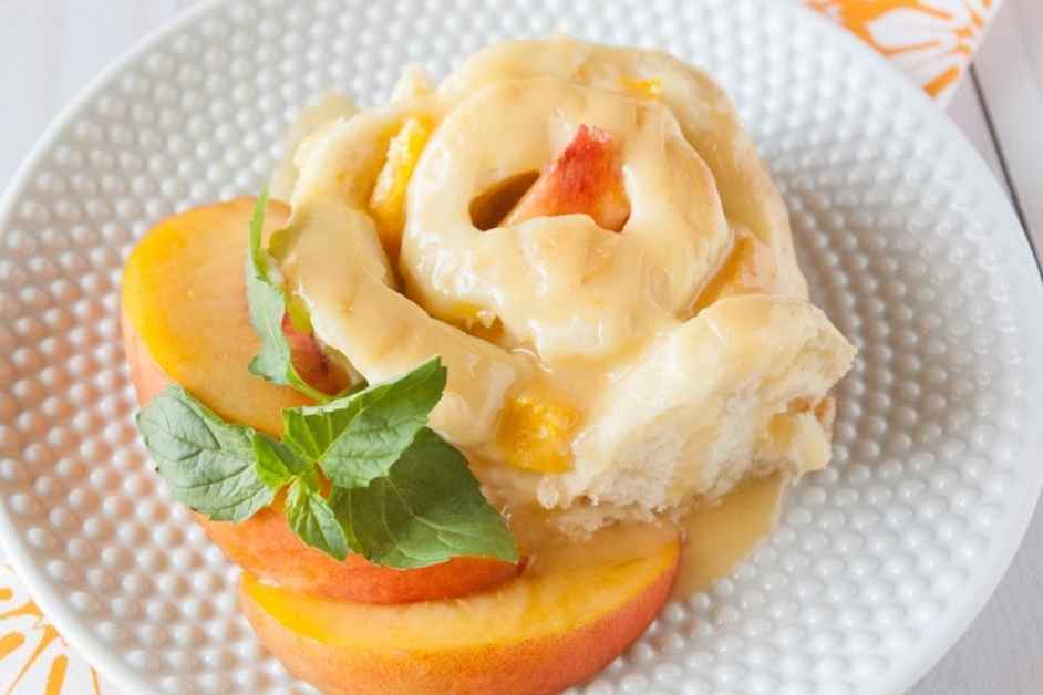 A Peach Sweet Roll on a white plate garnished with fresh peach slices and mint.