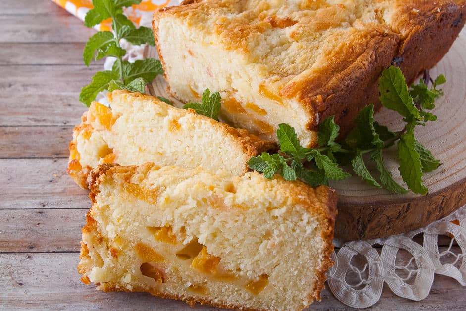 Loaf of fresh peach pound cake with two slices cut off and garnished with mint.