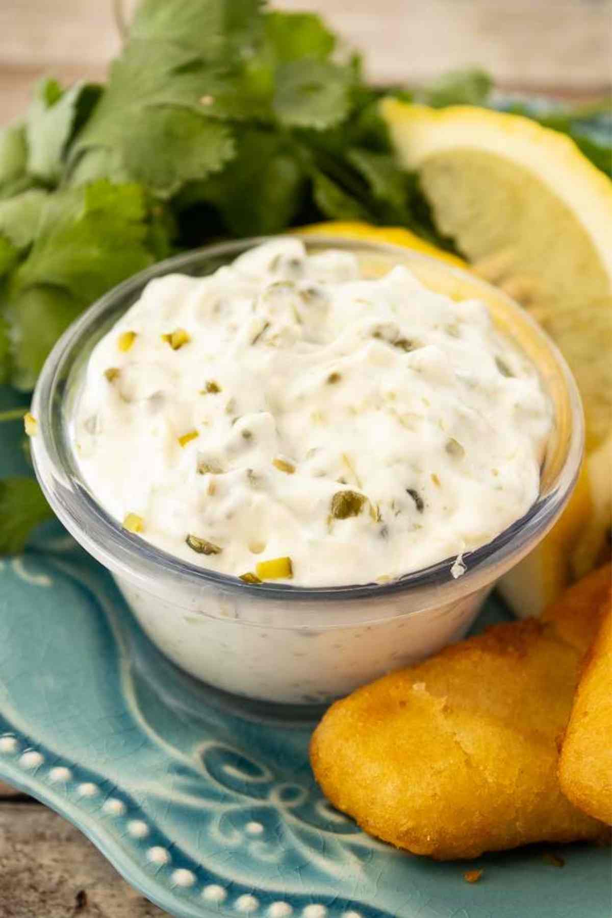 A dipping bowl filled with tartar sauce placed on a plate next to some fish fillets.