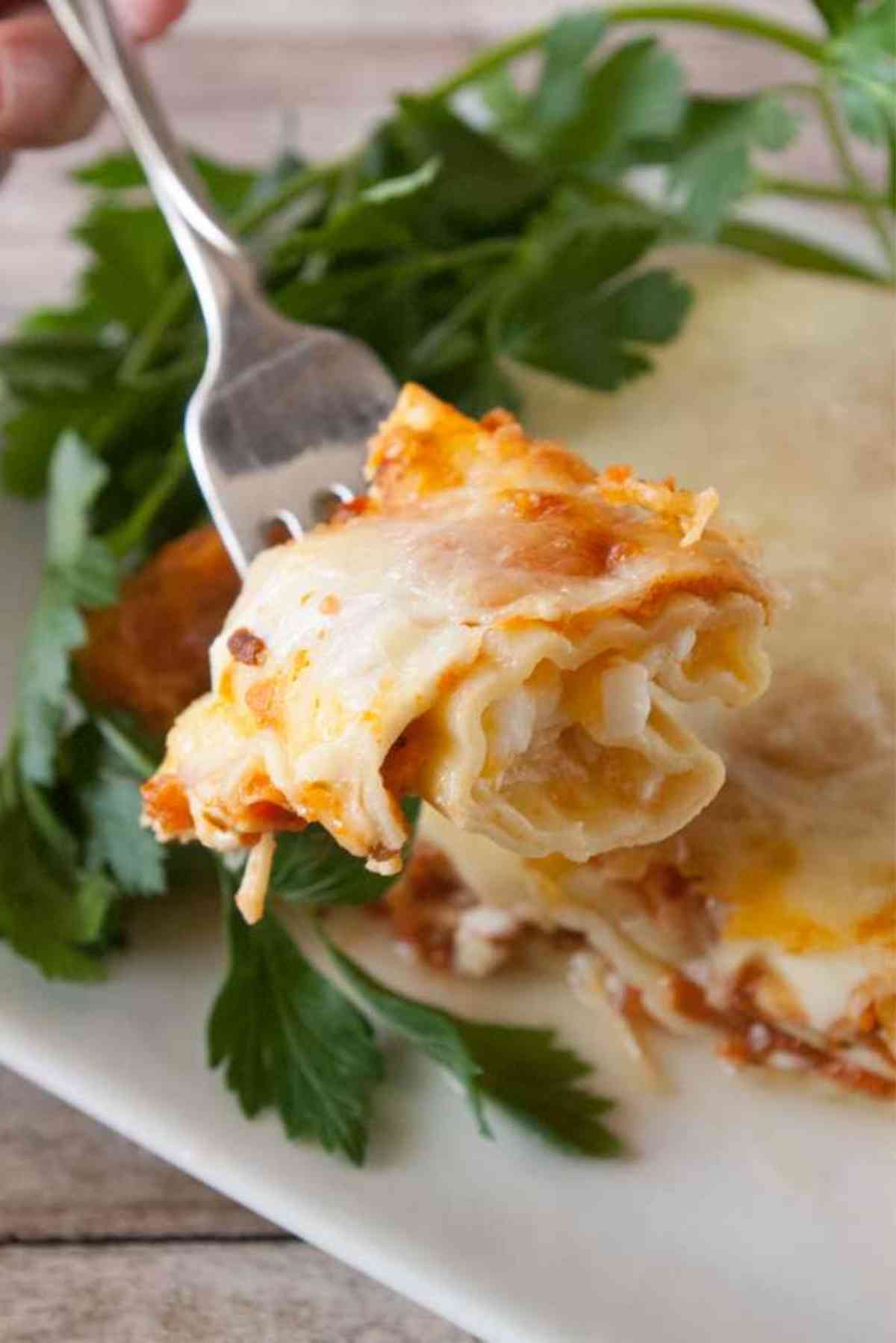 A fork lifting a bite of three cheese manicotti up from the plate.
