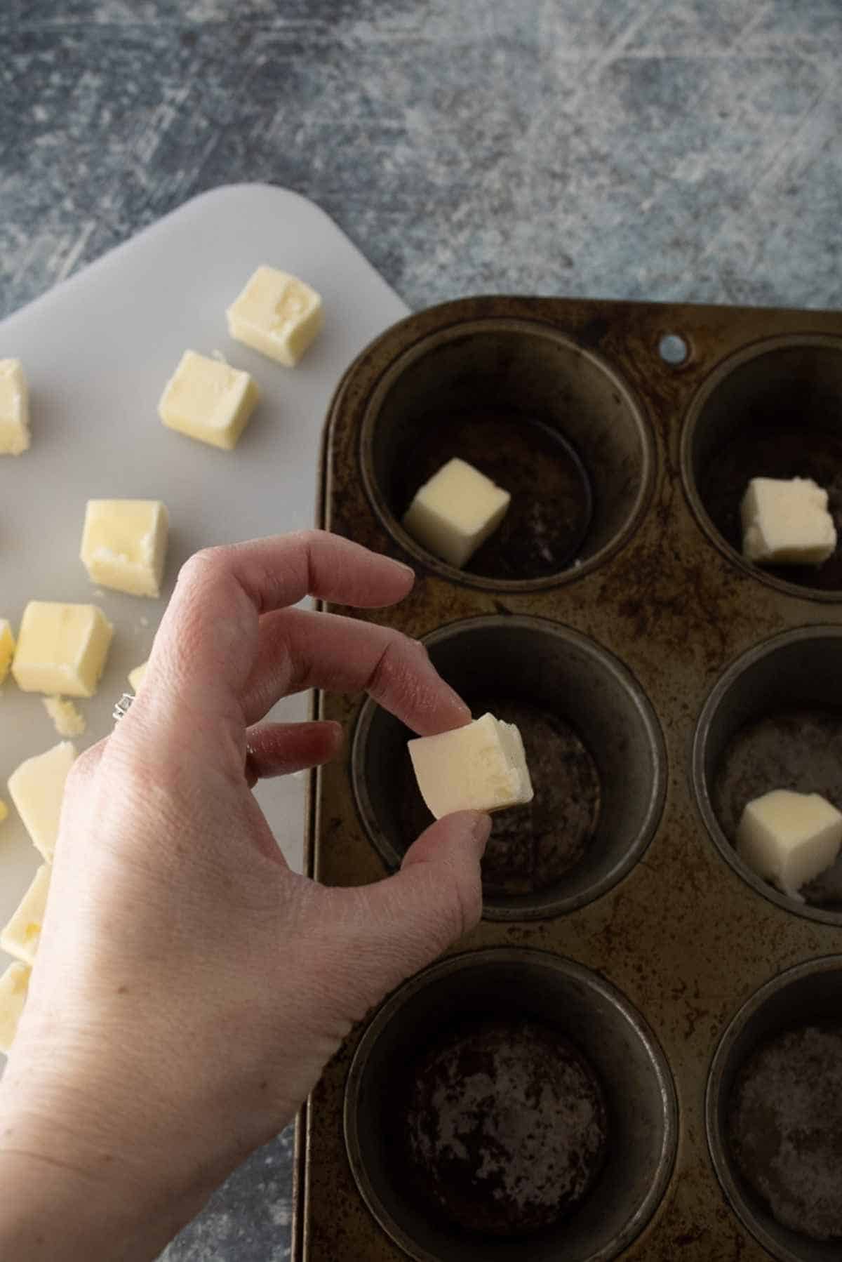 Butter pieces being added to the muffin tin.