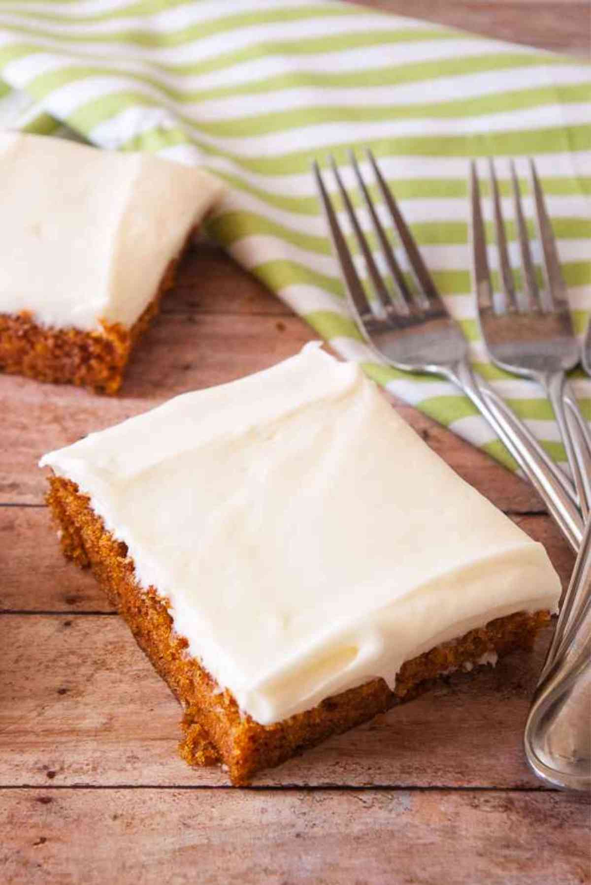 A slice of carrot sheet cake frosted with cream cheese frosting next to two forks.