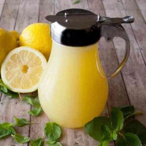 Lemon Cream Syrup next to fresh lemons and mint.