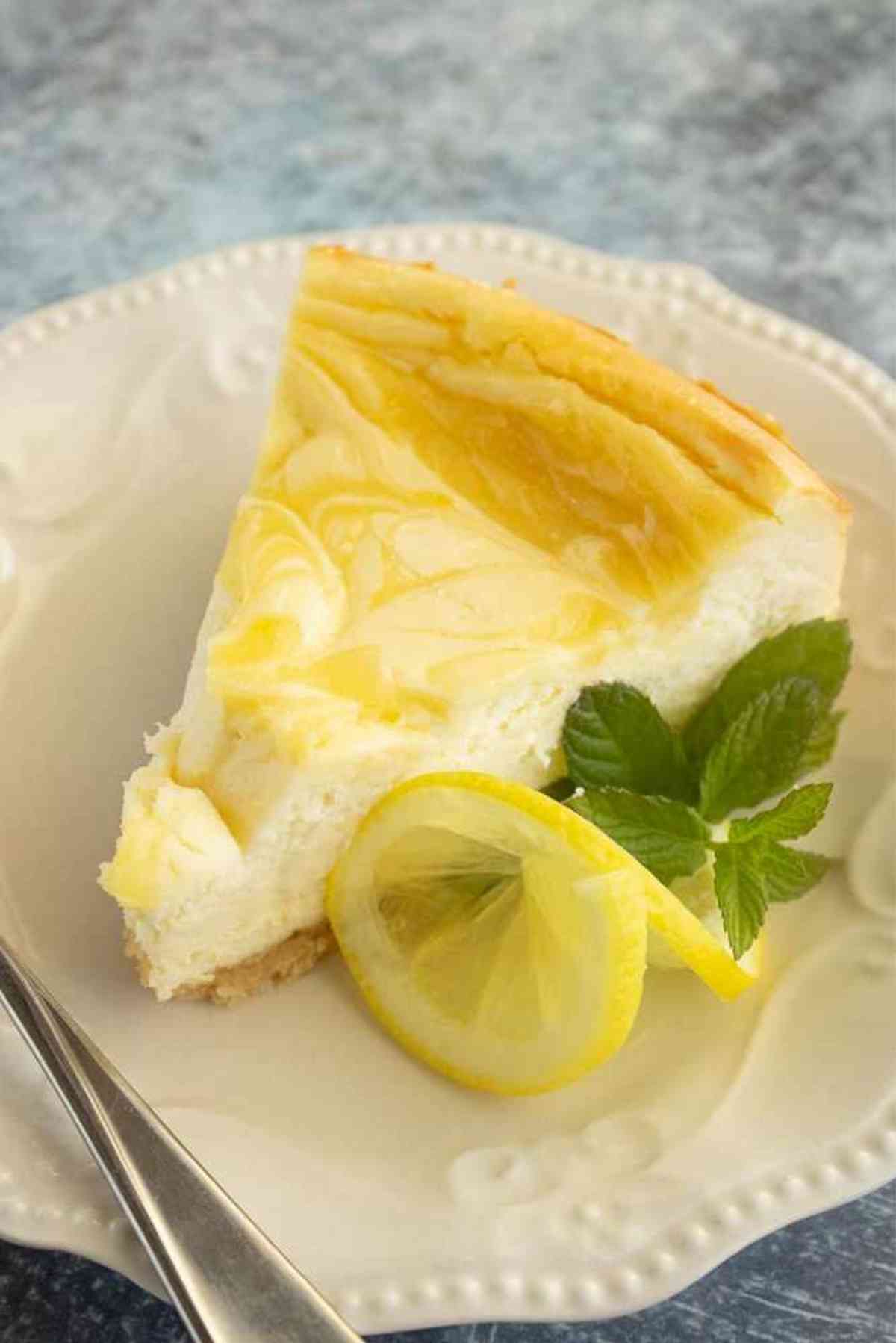 Slice of lemon swirl cheesecake garnished with lemon slice and mint.