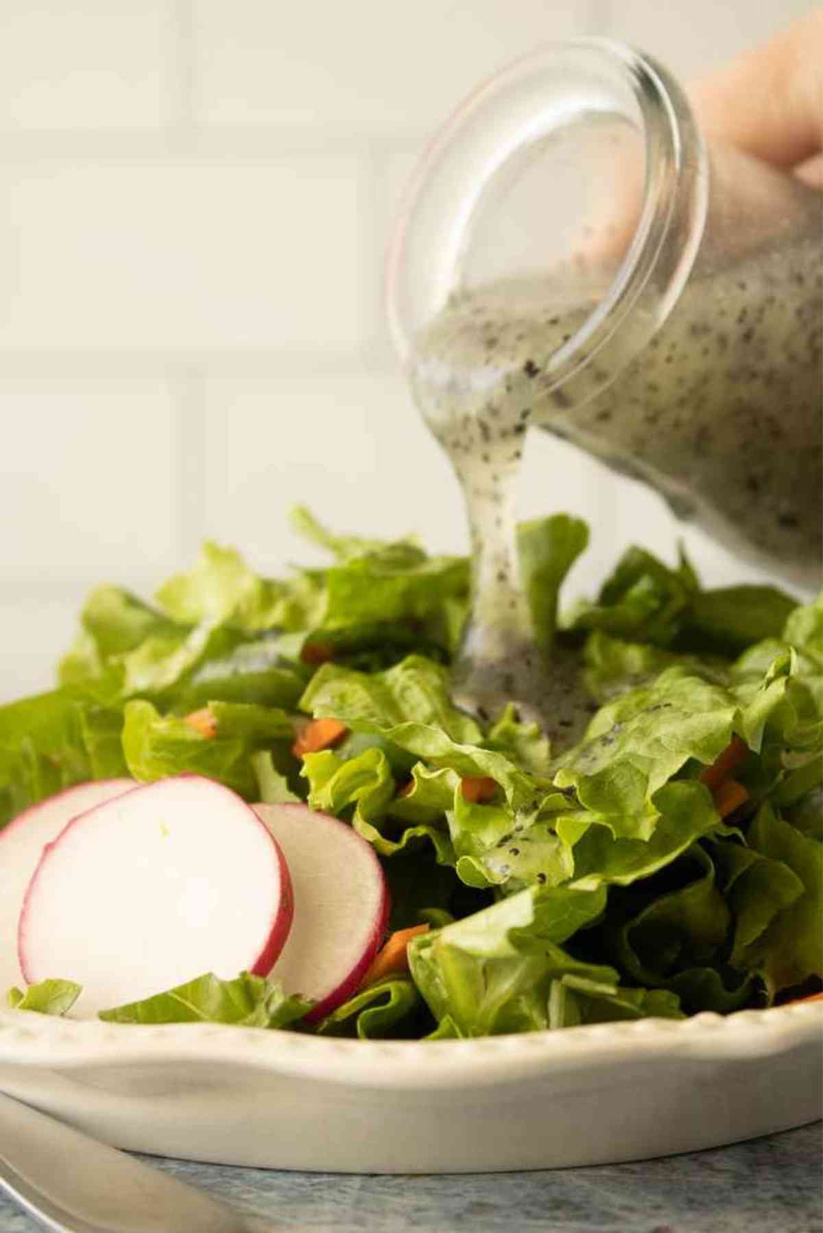 Poppy seed dressing being drizzled over a fresh green salad.