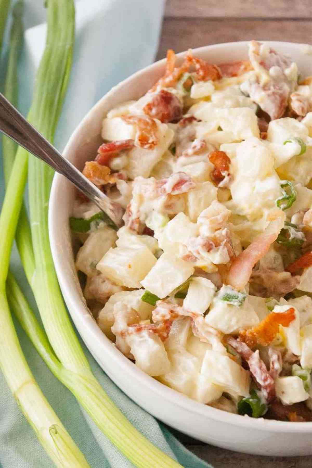 A bowlful of dill pickle potato salad garnished with green onions.