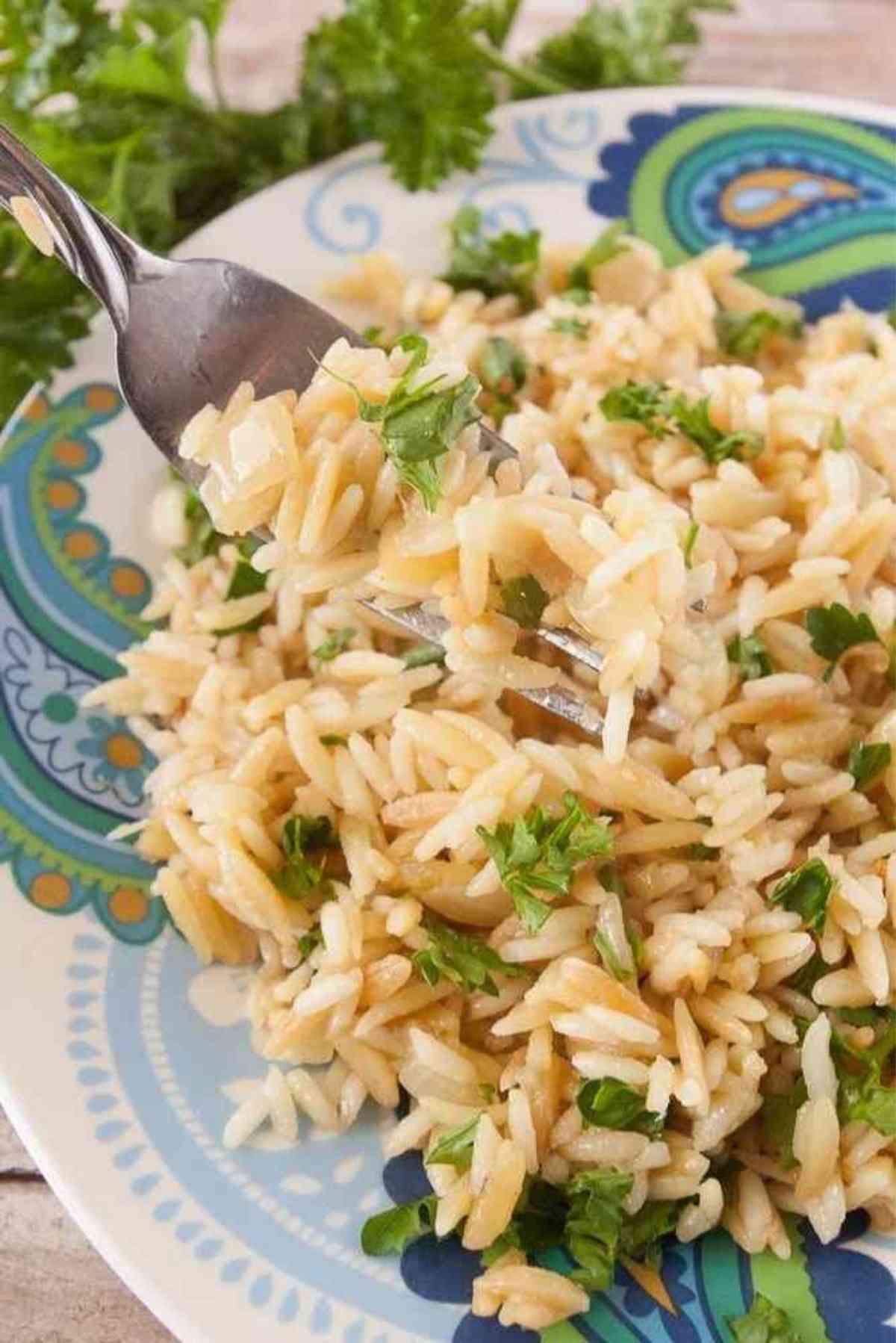 A forkful of orzo rice pilaf sprinkled with fresh parsley.