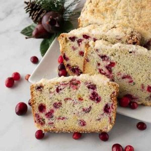 A baked loaf of cranberry poppy seed bread on a decorative plate garnished with fresh cranberries