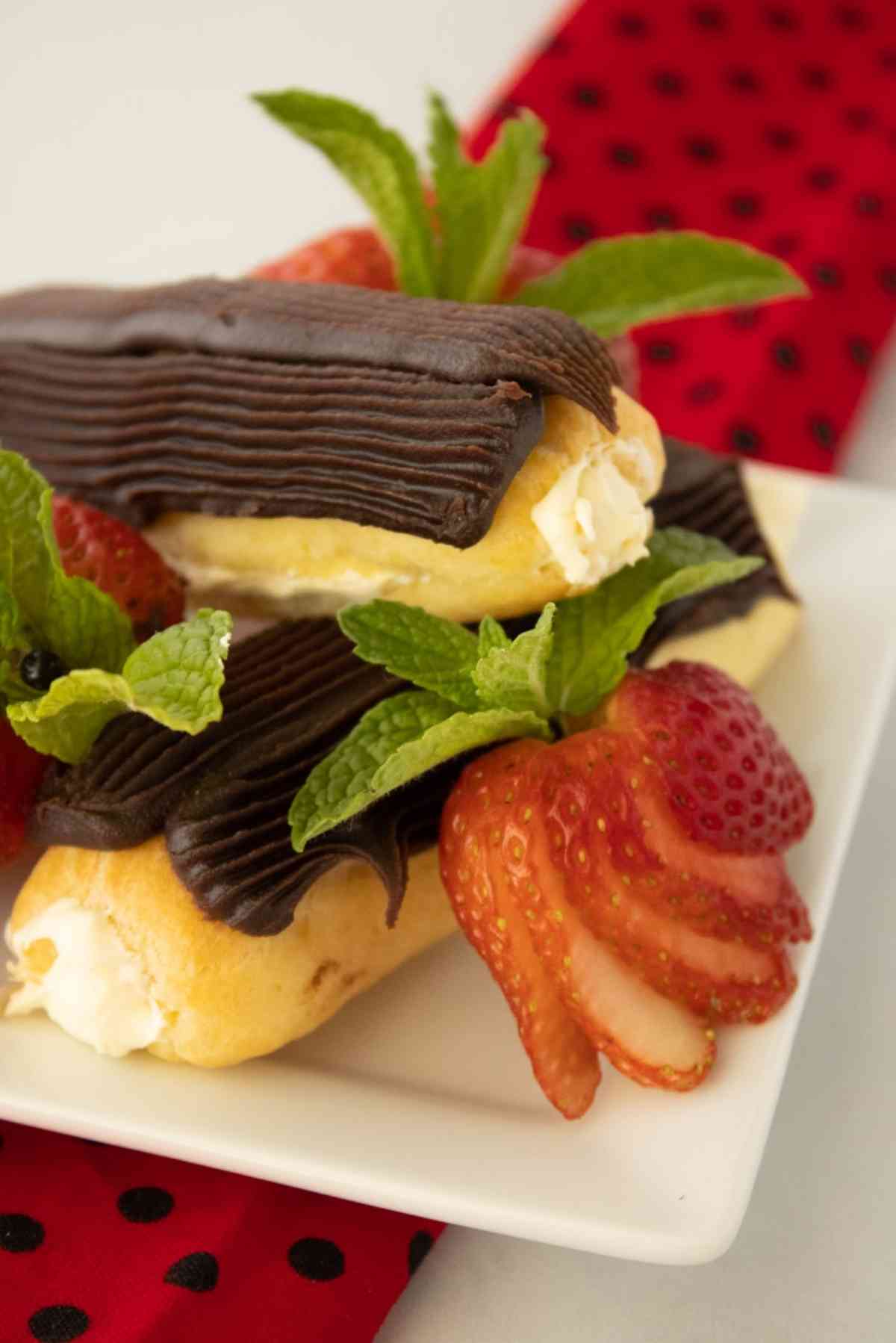 Mini eclairs topped with chocolate ganache and garnished with fresh mint and strawberries.