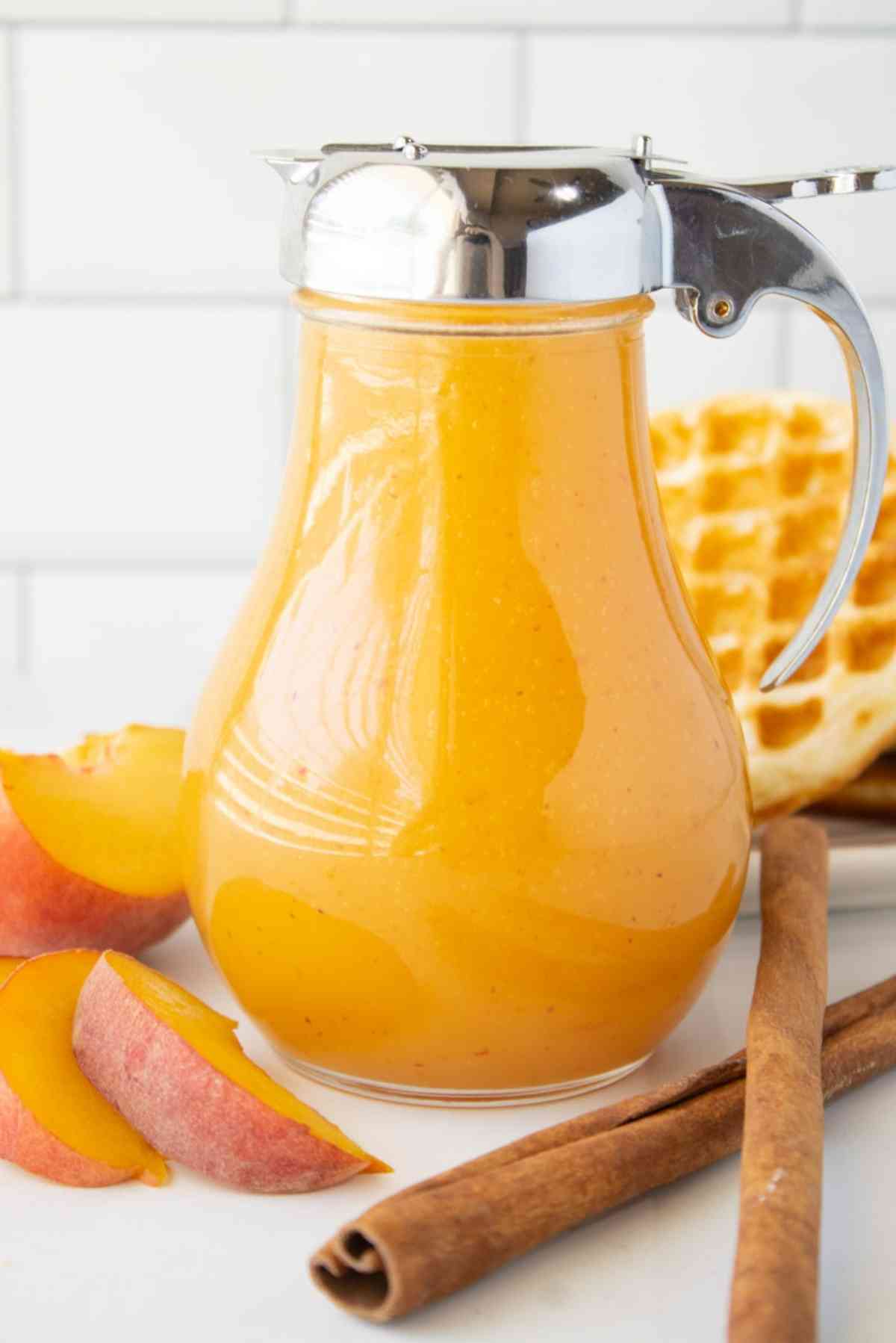 Bottle of fresh peach syrup by some waffles.