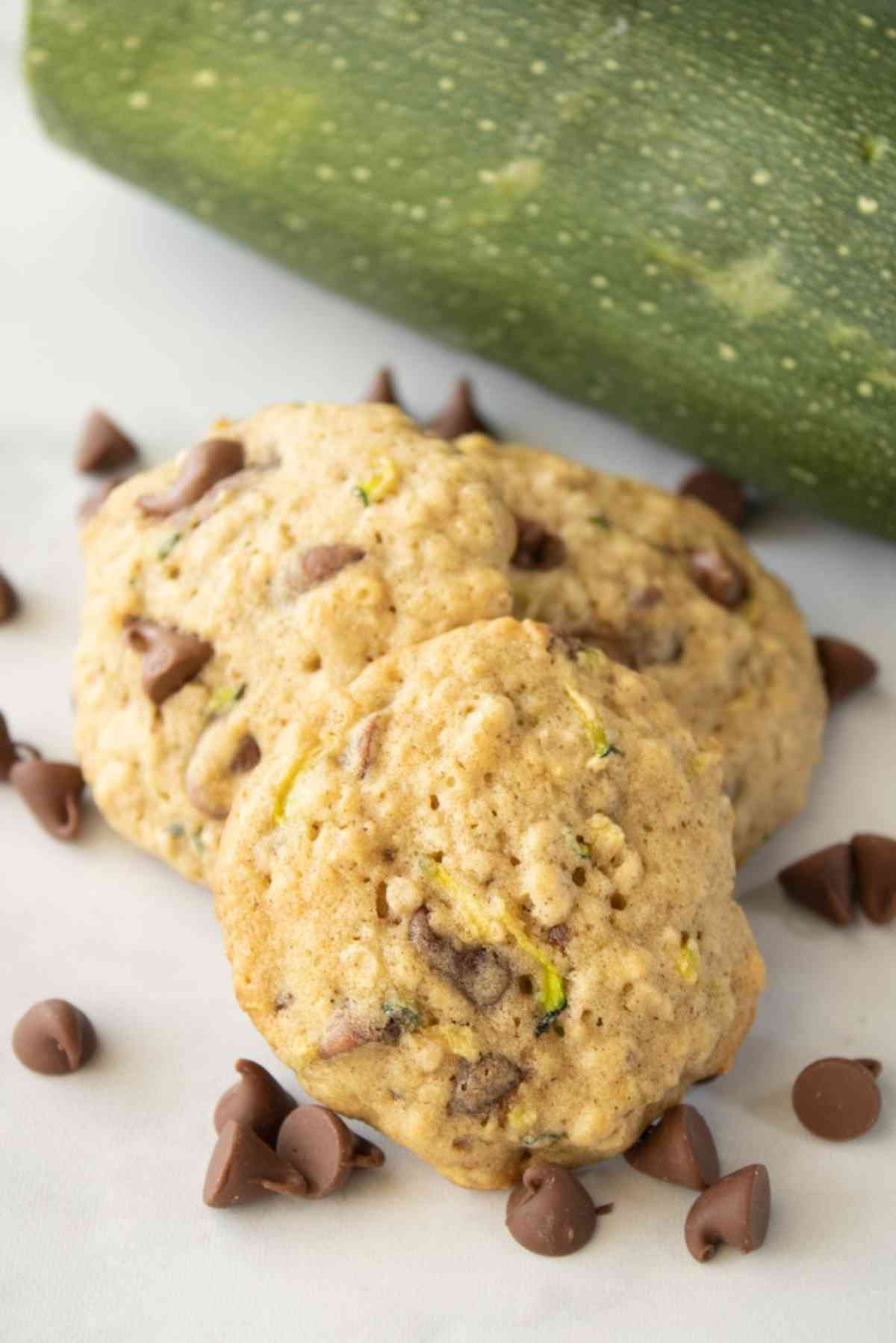 Pile of zucchini chocolate chip cookies next to a zucchini.