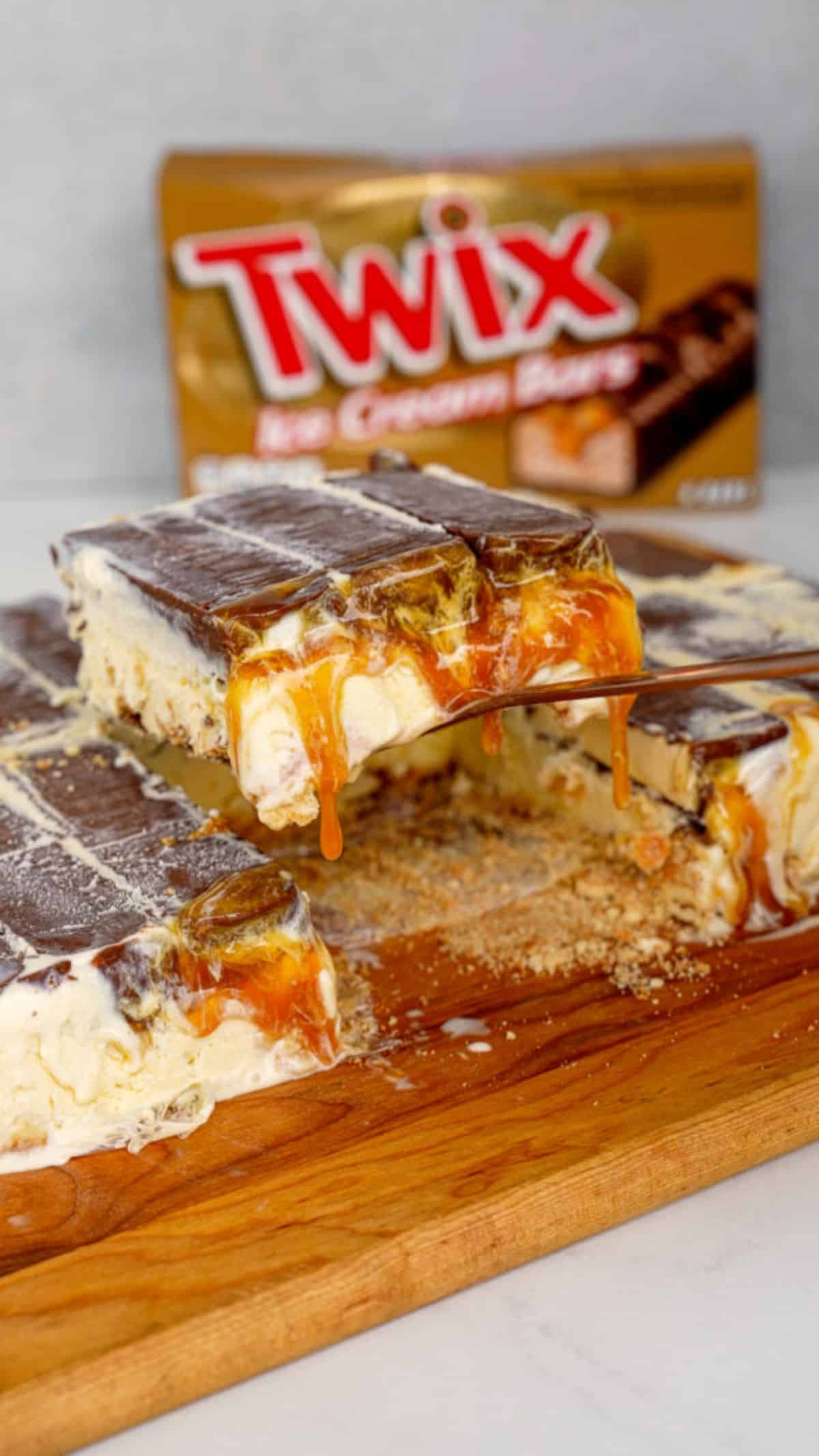 Twix Ice Cream Bar Cake on a wooden tray picked by a spatula.