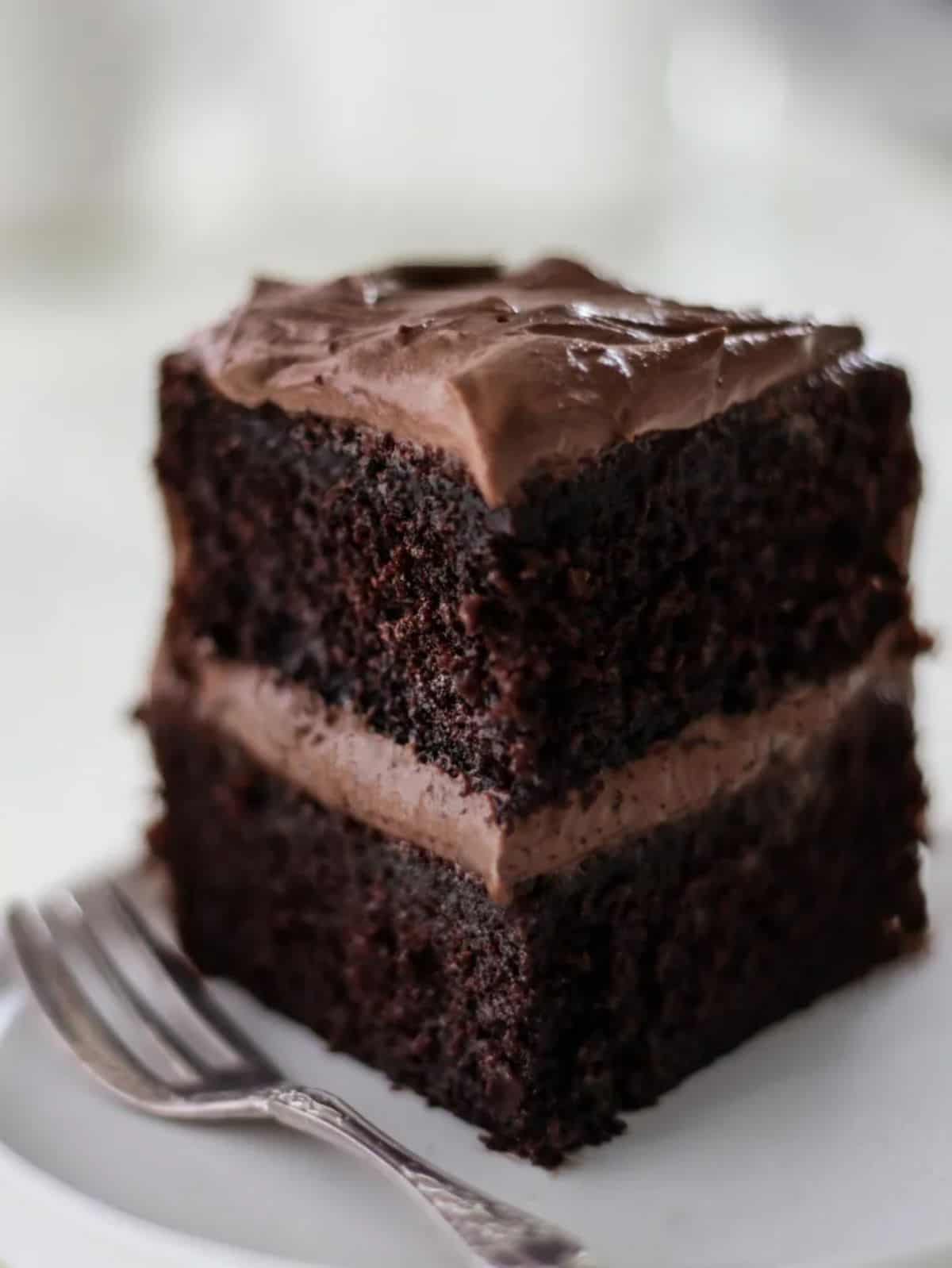 A piece of cake with Chocolate Cream Cheese Frosting on a white plate with a fork.