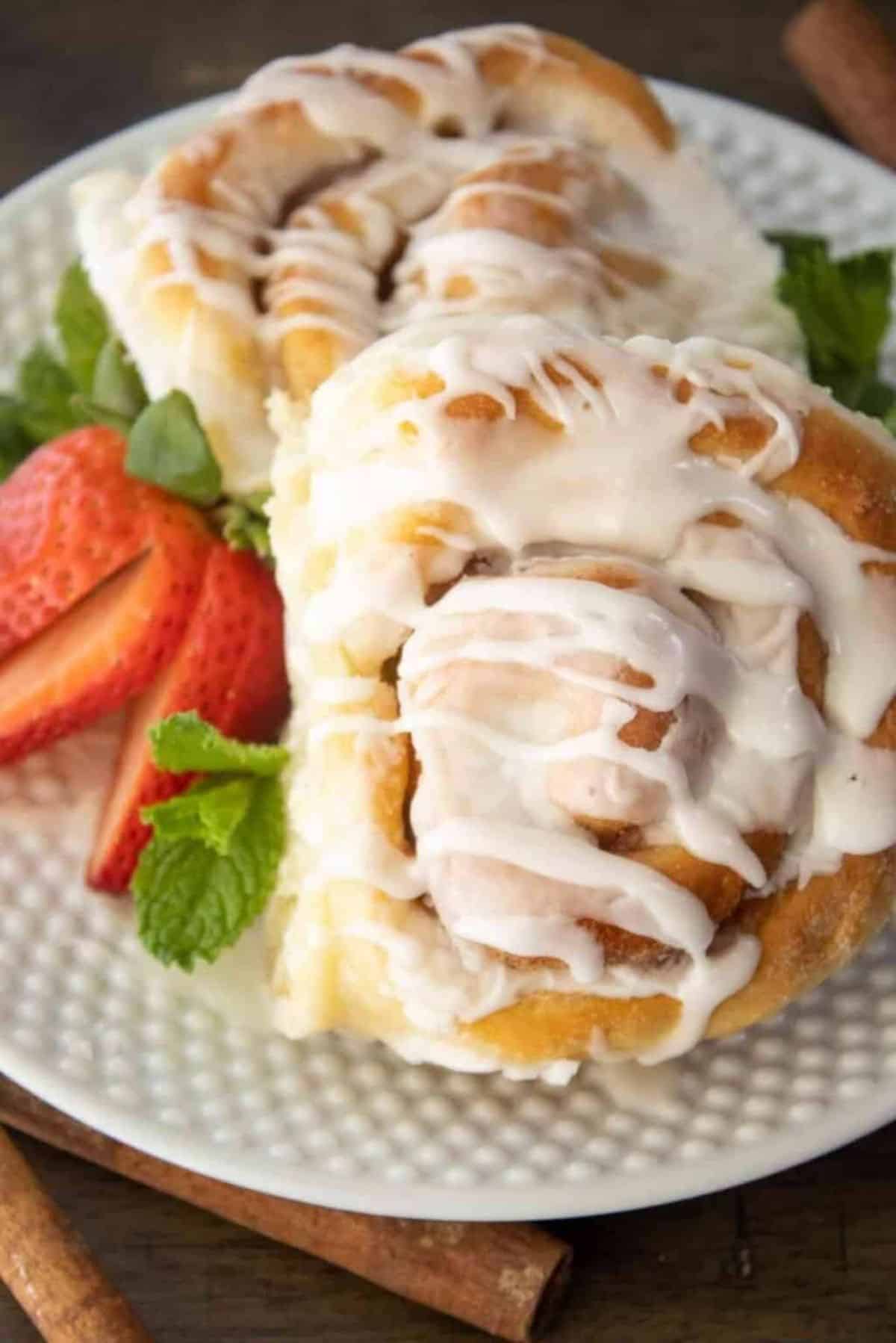 Cinnamon Rolls with a sliced strawberry on a white plate.