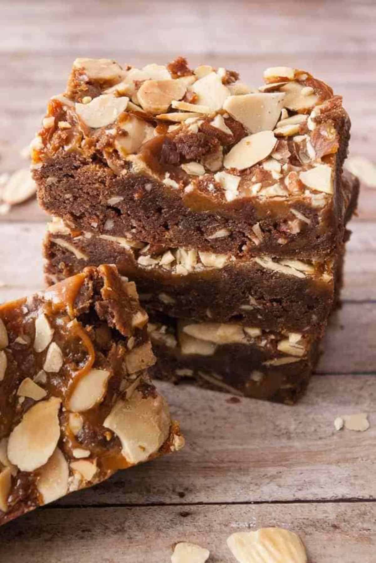 A pilfe of delicious Caramel Fudge Nut Brownies on a wooden table.