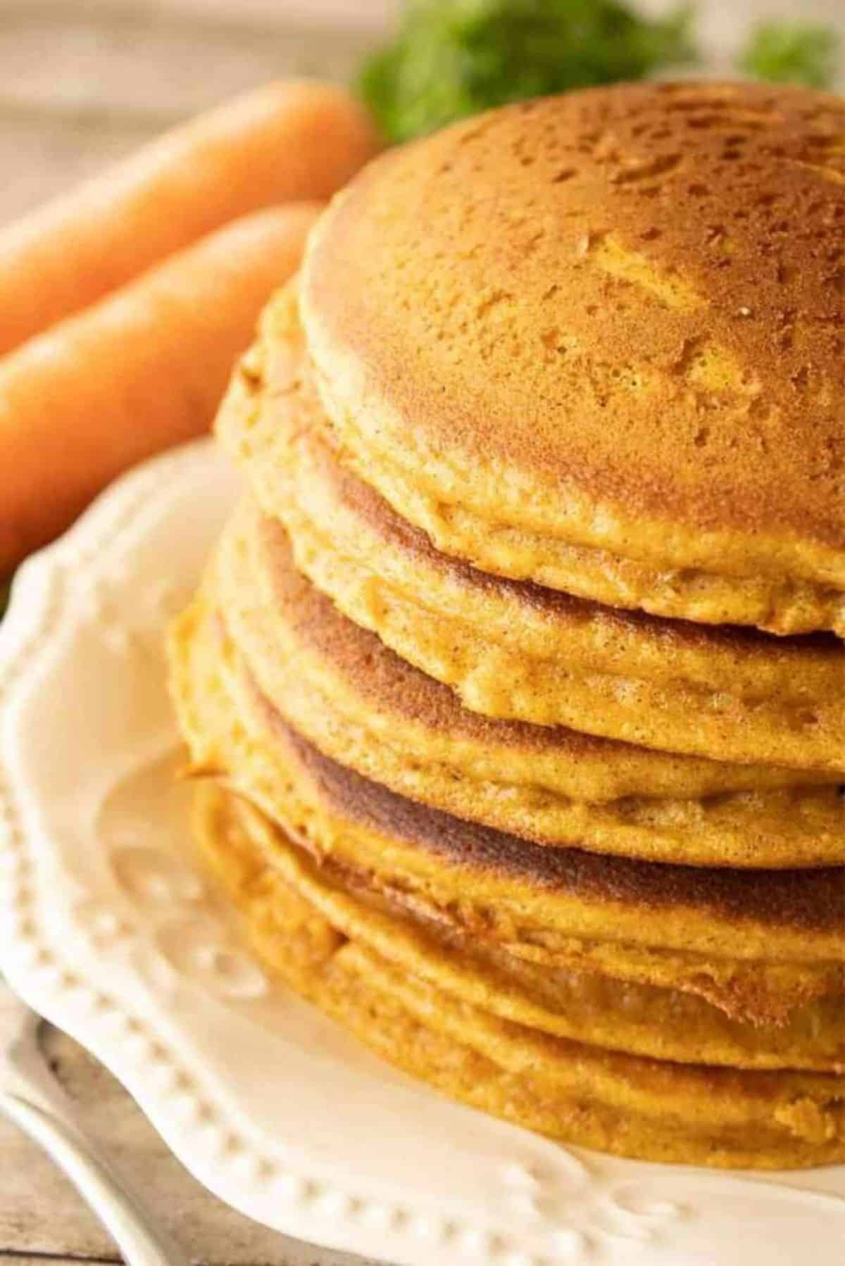 A pile of Carrot Cake Pancakes with Cream Cheese Syrup  on a white plate.