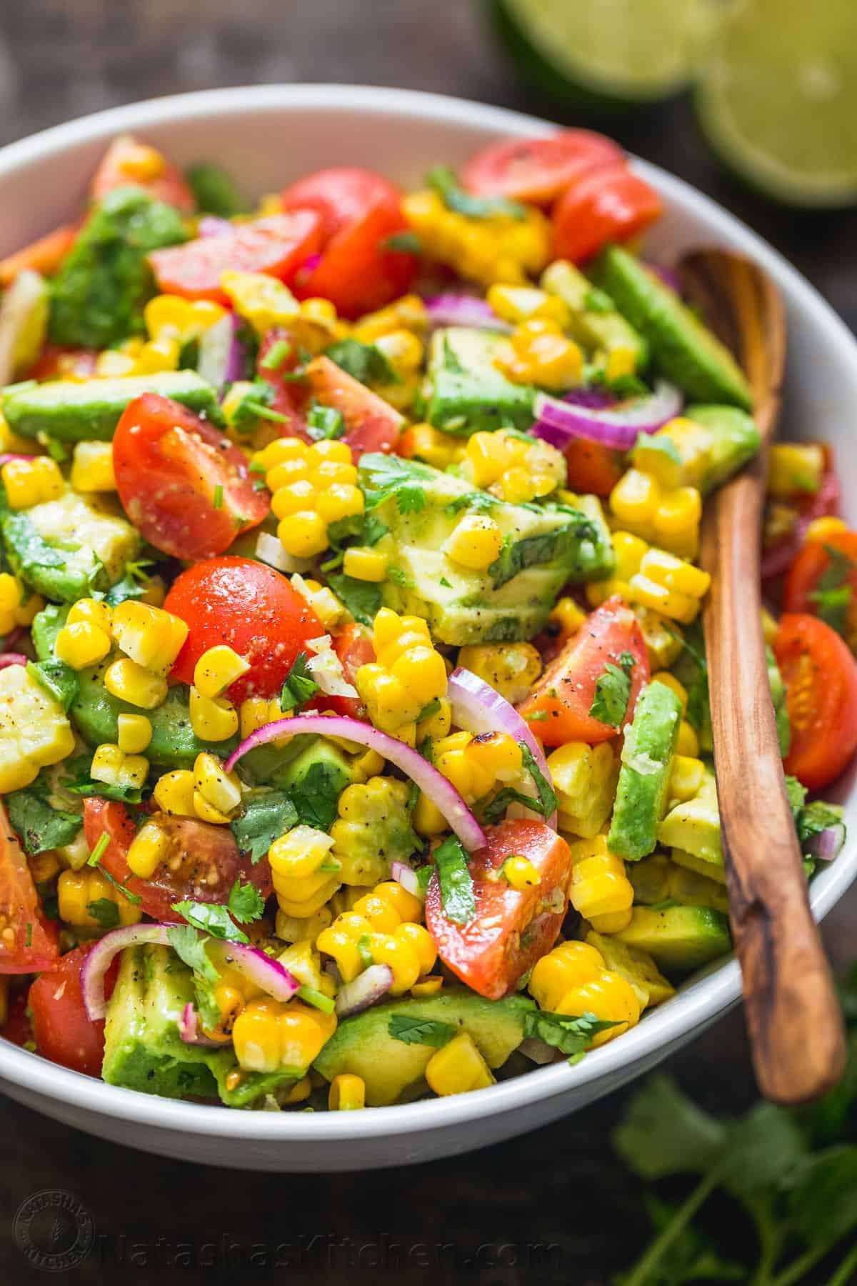 Avocado Corn Salad in a white bowl with a wooden spoon.