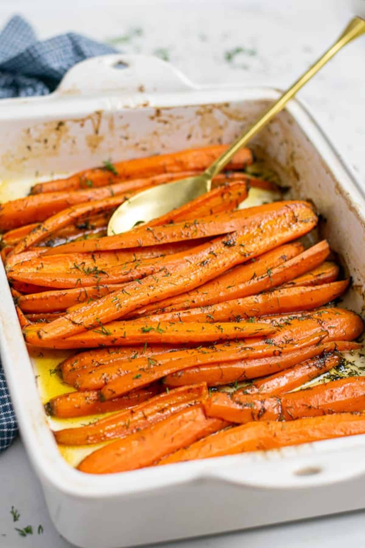 Dill and Garlic Roasted Carrots in a white casserole with a spoon.