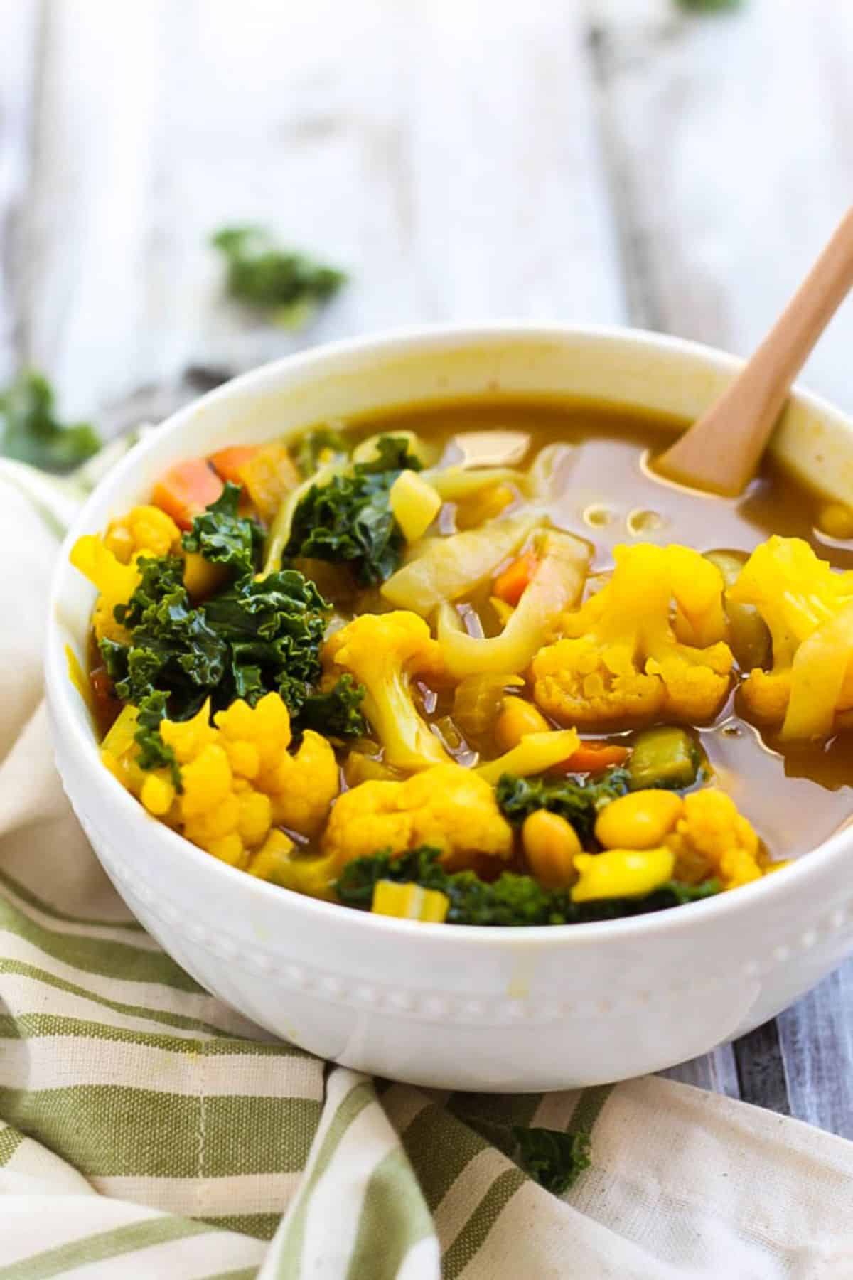 Turmeric Cauliflower Soup in a white bowl with a wooden spoon.