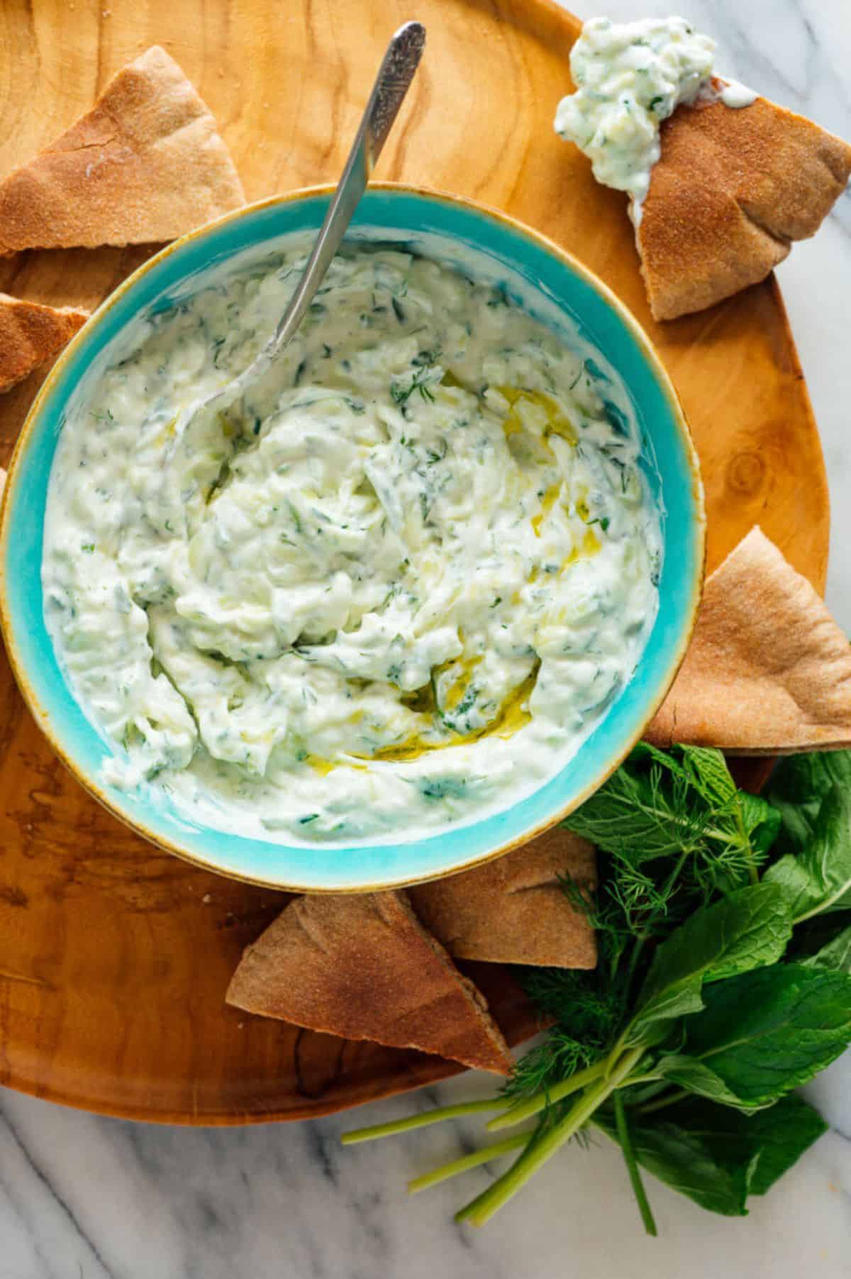 Tzatziki in a bliue bow on a wooden tray.