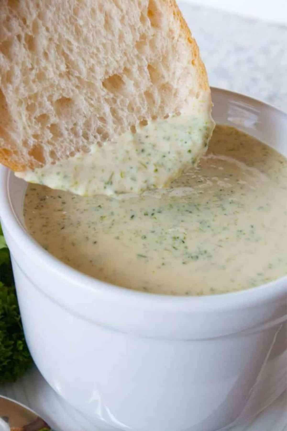 A slice of bread dipped in a bowl of Broccoli Cheese Soup.