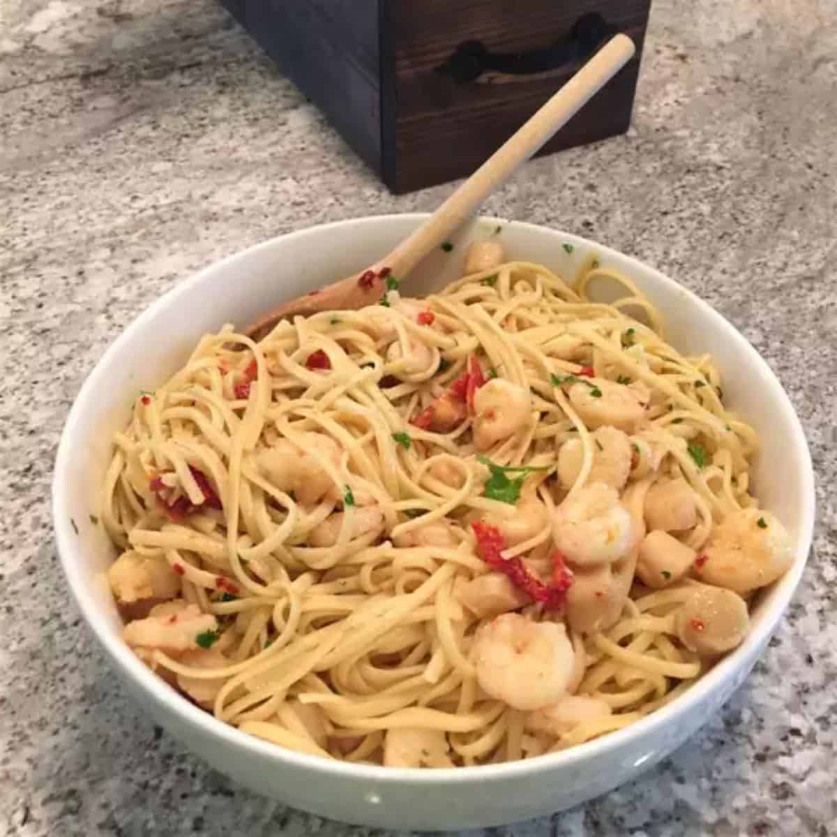 Linguine with Seafood and Sun-dried Tomatoes in a white bowl with a wooden spoon.