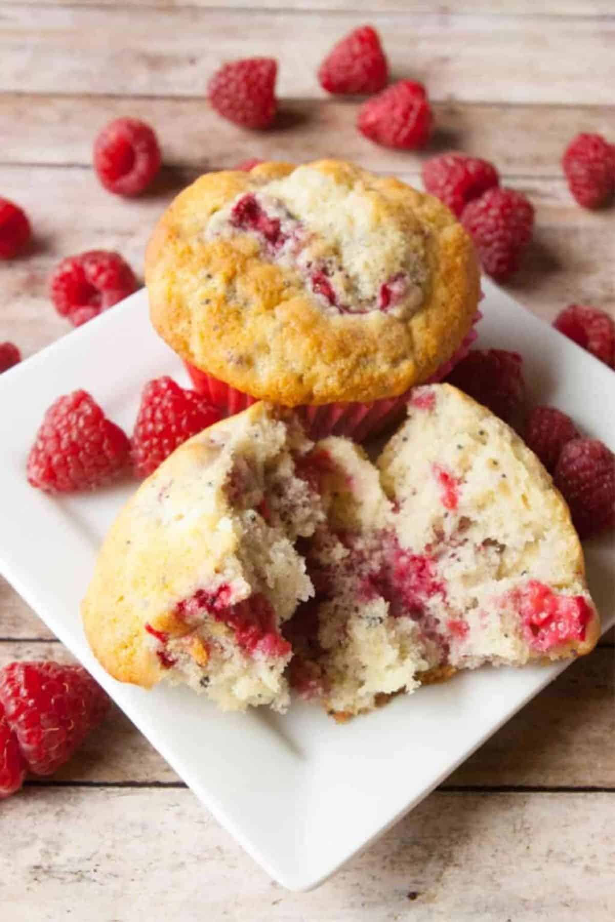 Delicious Raspberry Poppy Seed Muffins on a white plate with ripe rapsberries scattered around.