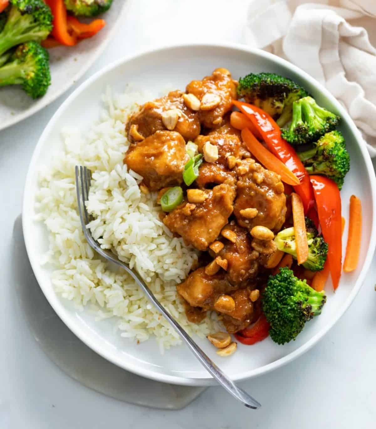 Peanut Butter Chicken with rice and veggies on a white plate.