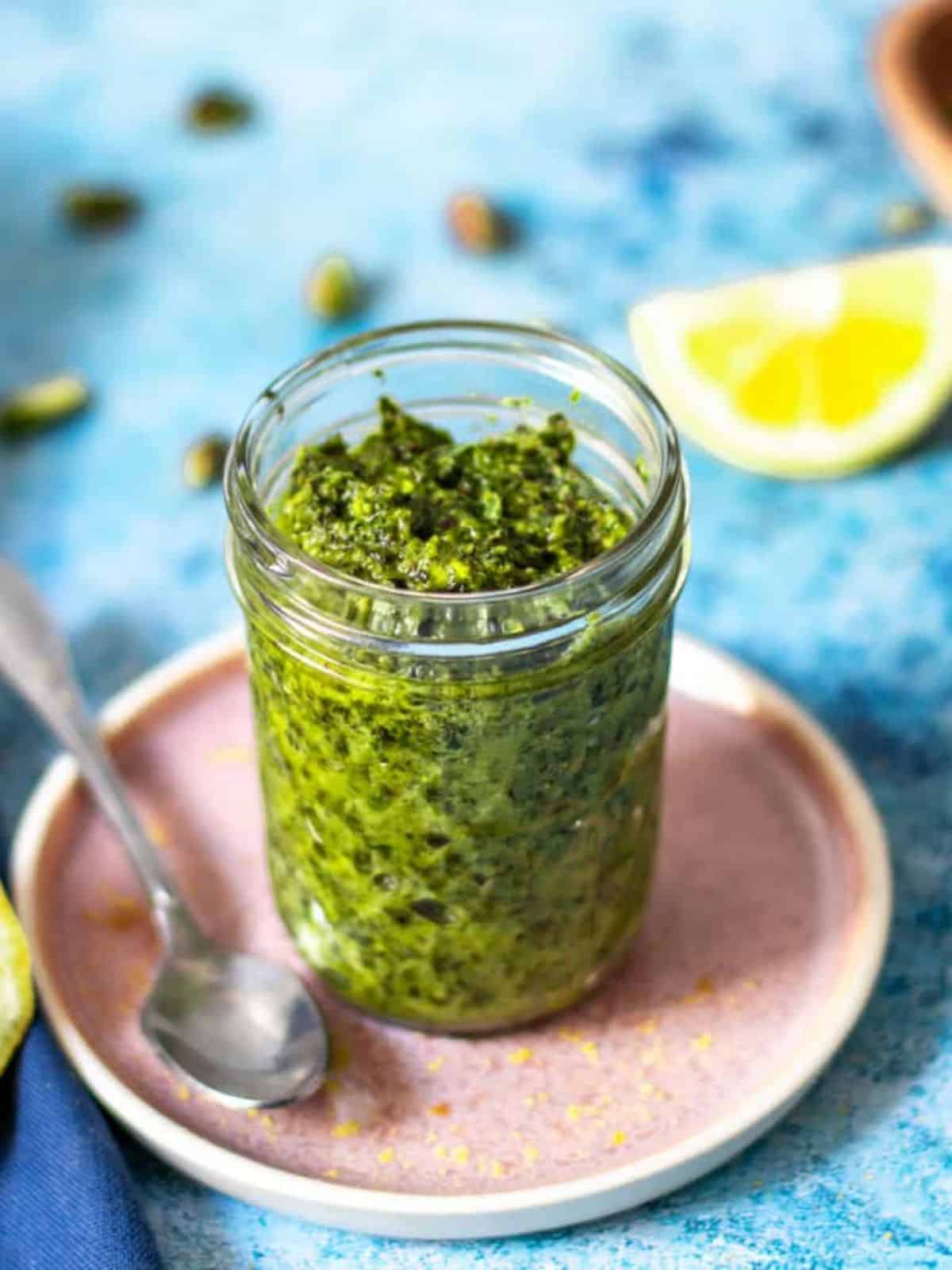 Pistachio Pesto in a glass jar on a small plate.