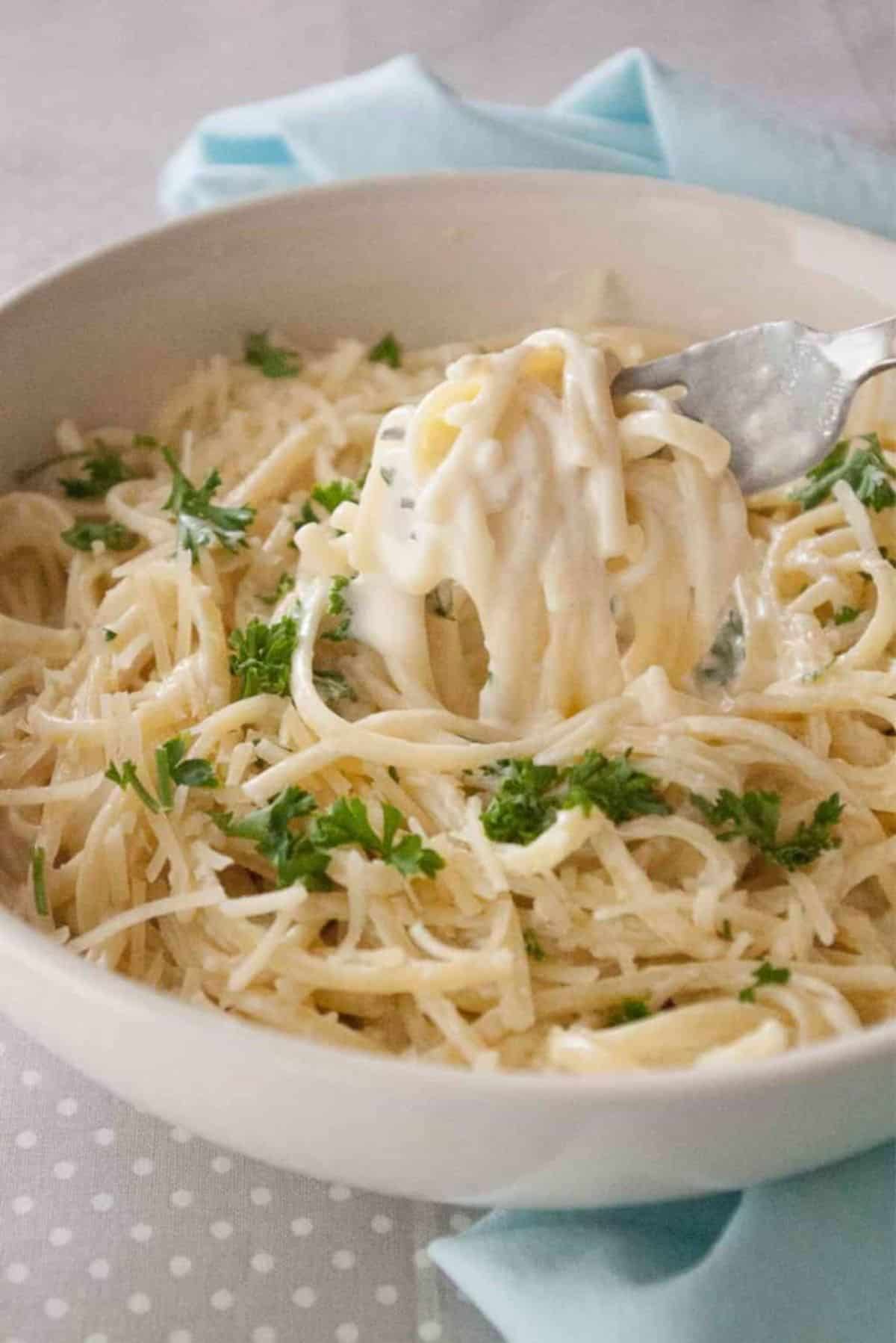 Easy Alfredo Sauce with pasta in a white bowl picked with a fork.