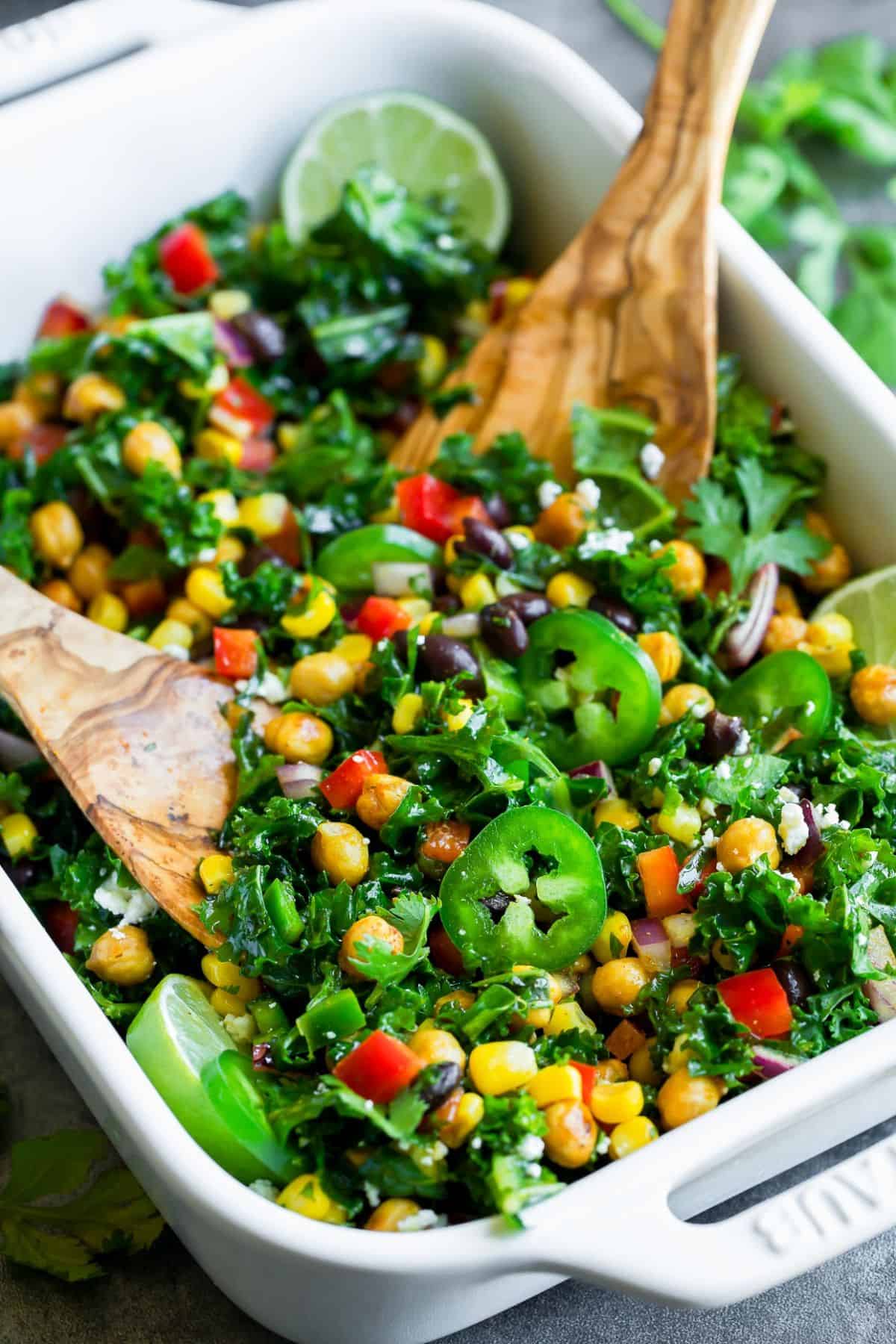 Mexican Kale Salad with Zesty Cilantro Lime Dressing in a white casserole with two wooden spatulas.