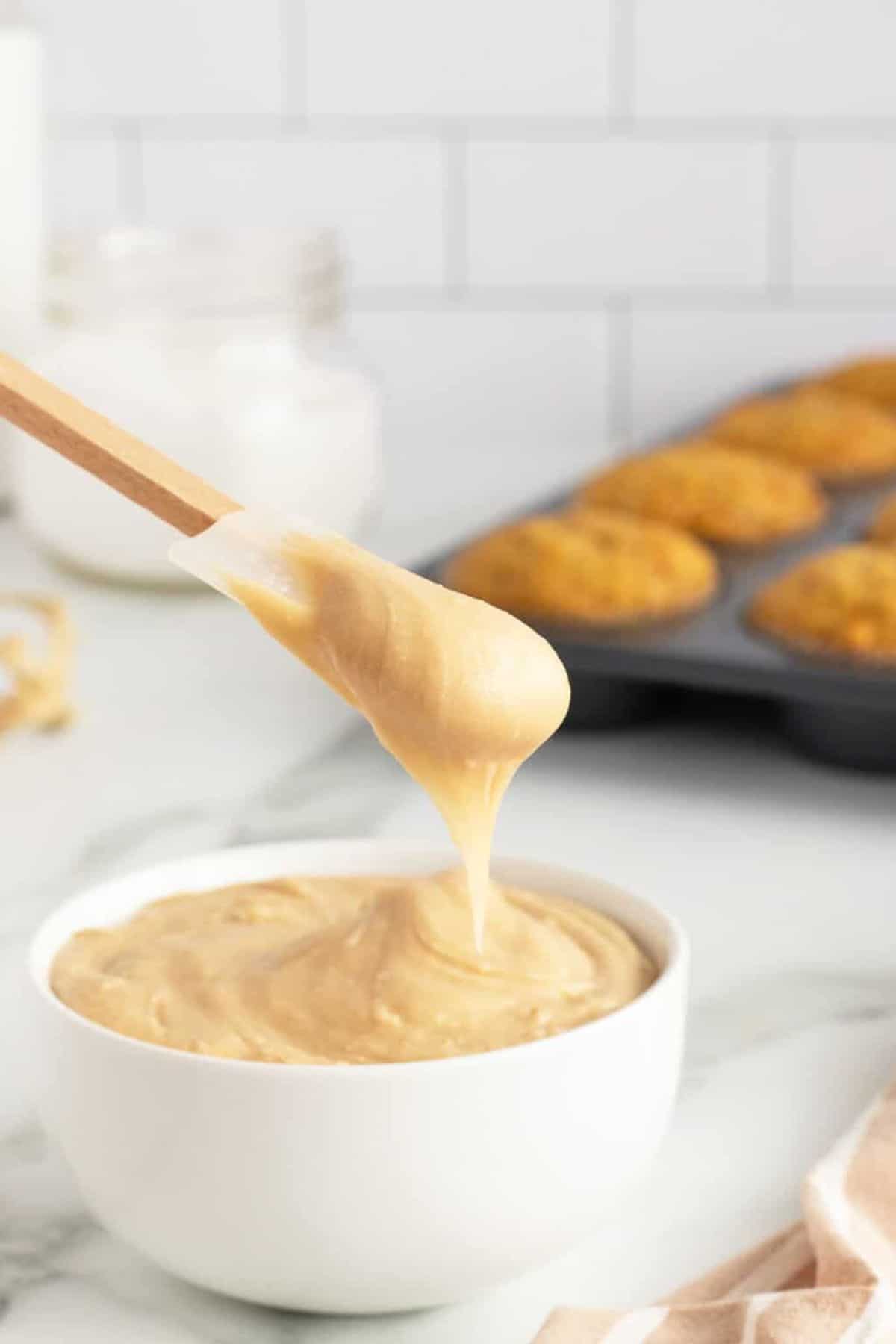 Maple Frosting in a white bowl and on a wooden spatula.
