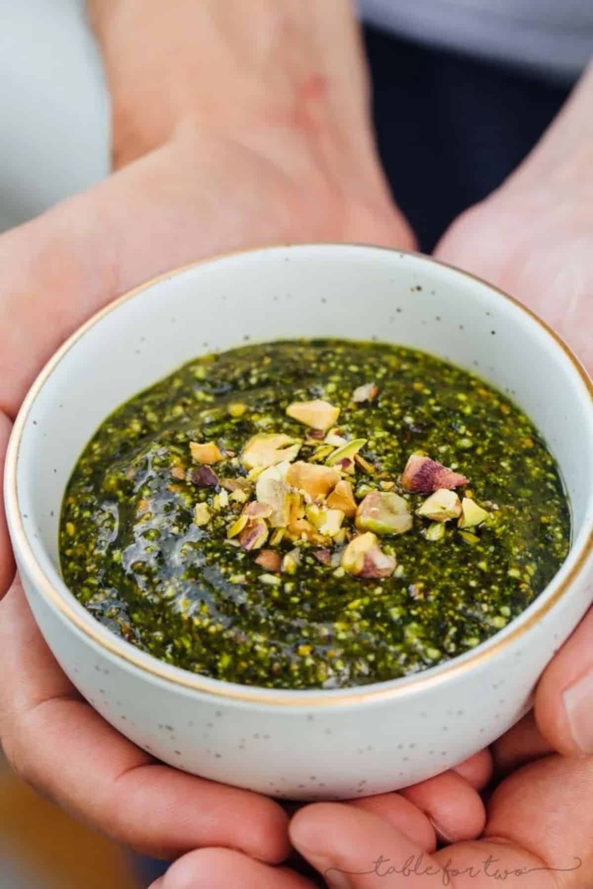 Pistachio Mint Pesto in a small bowl held by hands.