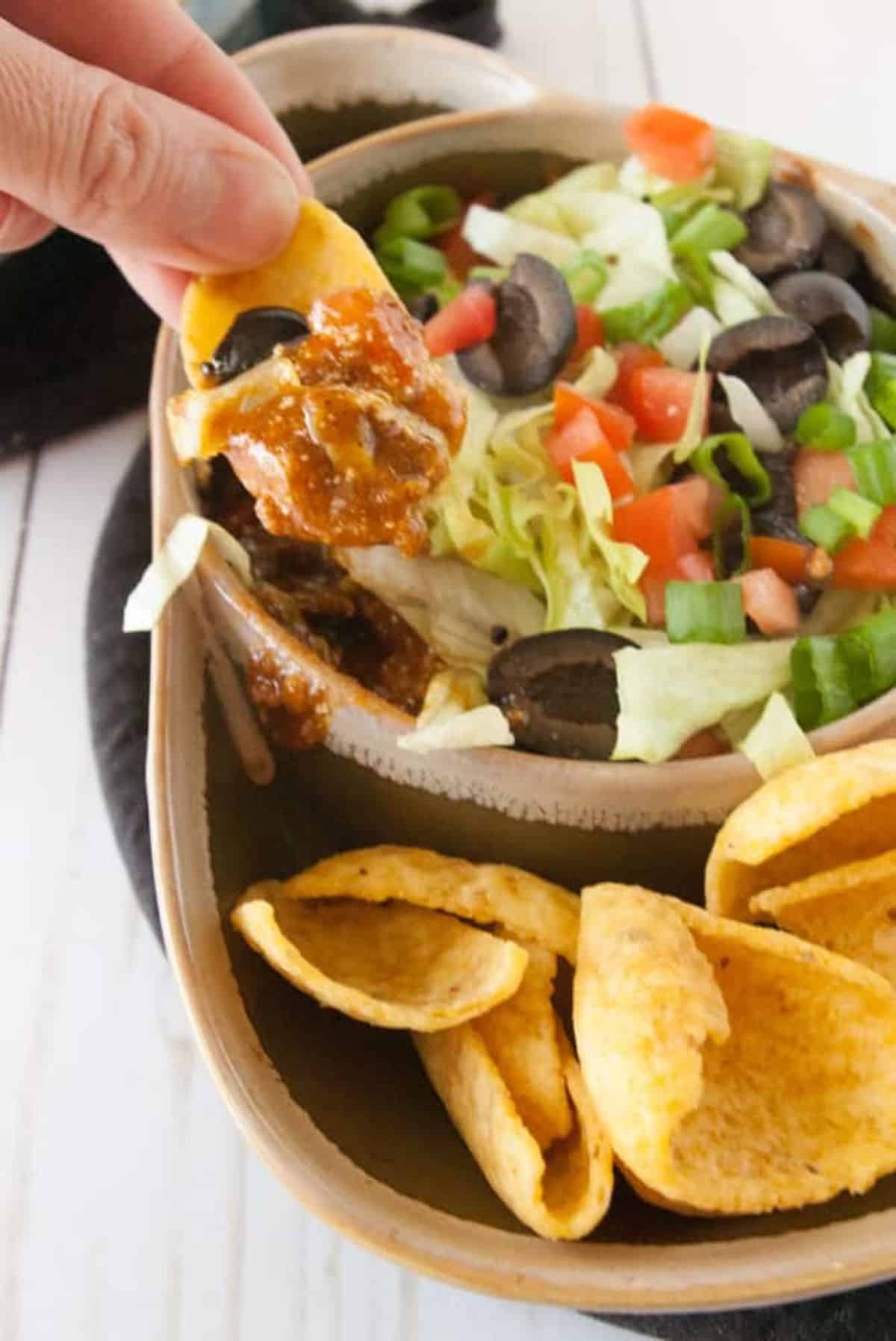 Chip dipped in a Hot Taco Chili Dip held by hand,