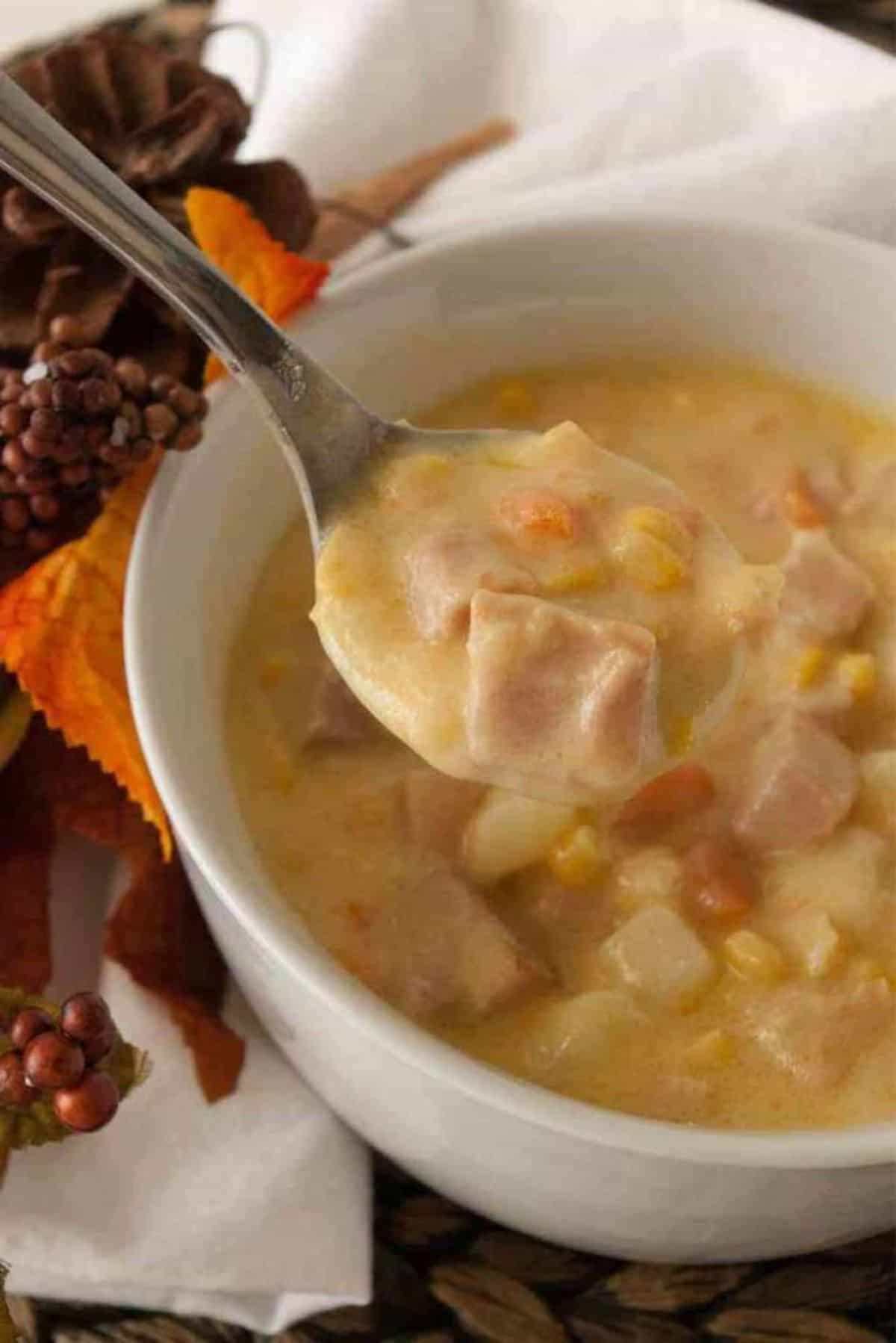 Cheesy Ham and Potato Soup in a white bowl picked with a spoon.