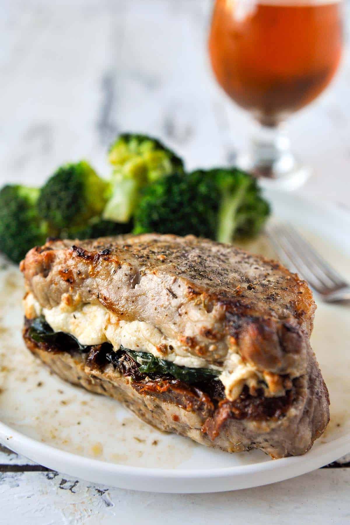 Delicious Stuffed Prok Chops with Sun-dried Tomatoes, Spinach & Cheese on a white plate.