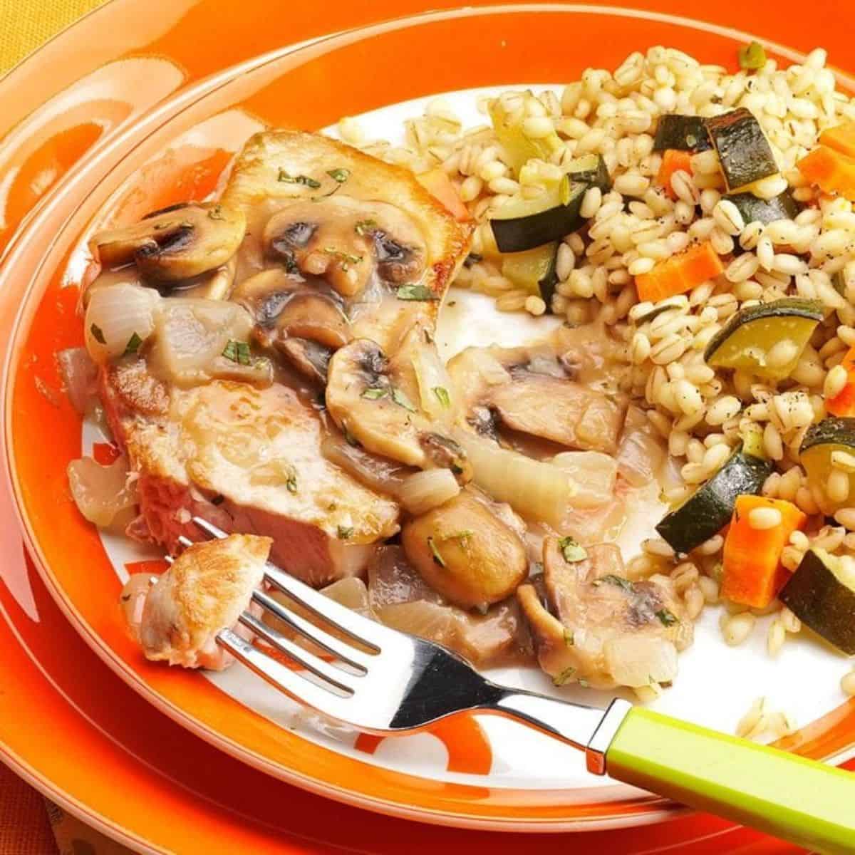 Delicious Pork Chops With Mushroom-tarragon Sauce on a red plate with a fork.