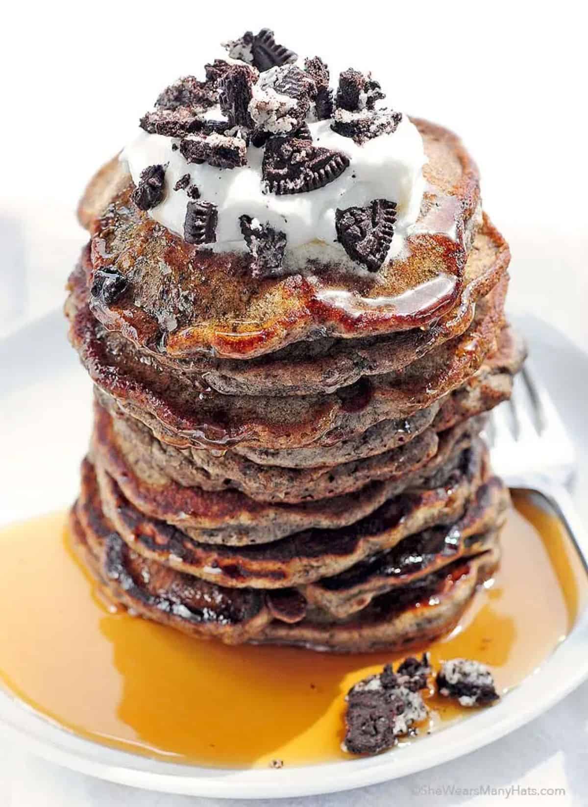 A pile of delicious Oreo Pancakes on a white plate with a fork.
