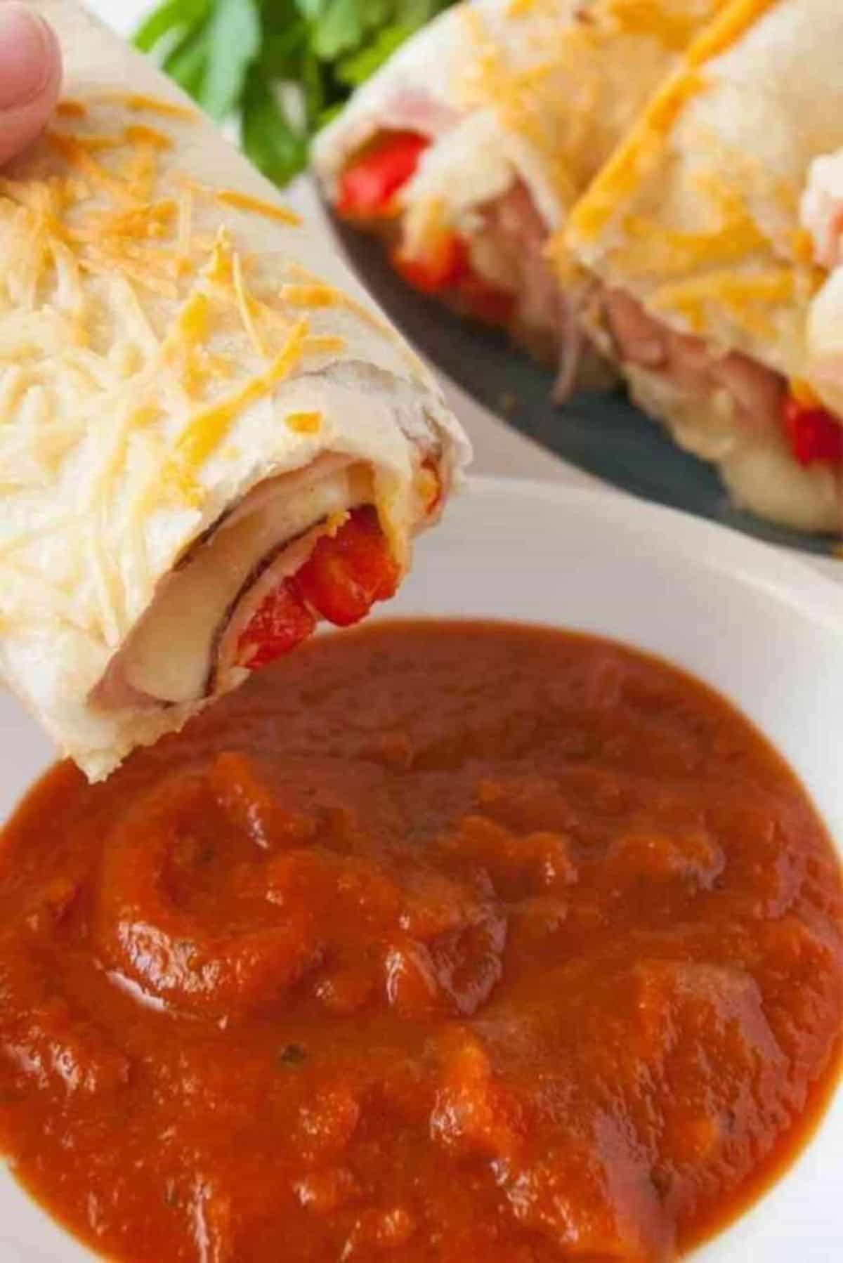 Baked Ham and Cheese Roll-Up held by hand over a bowl of dip.