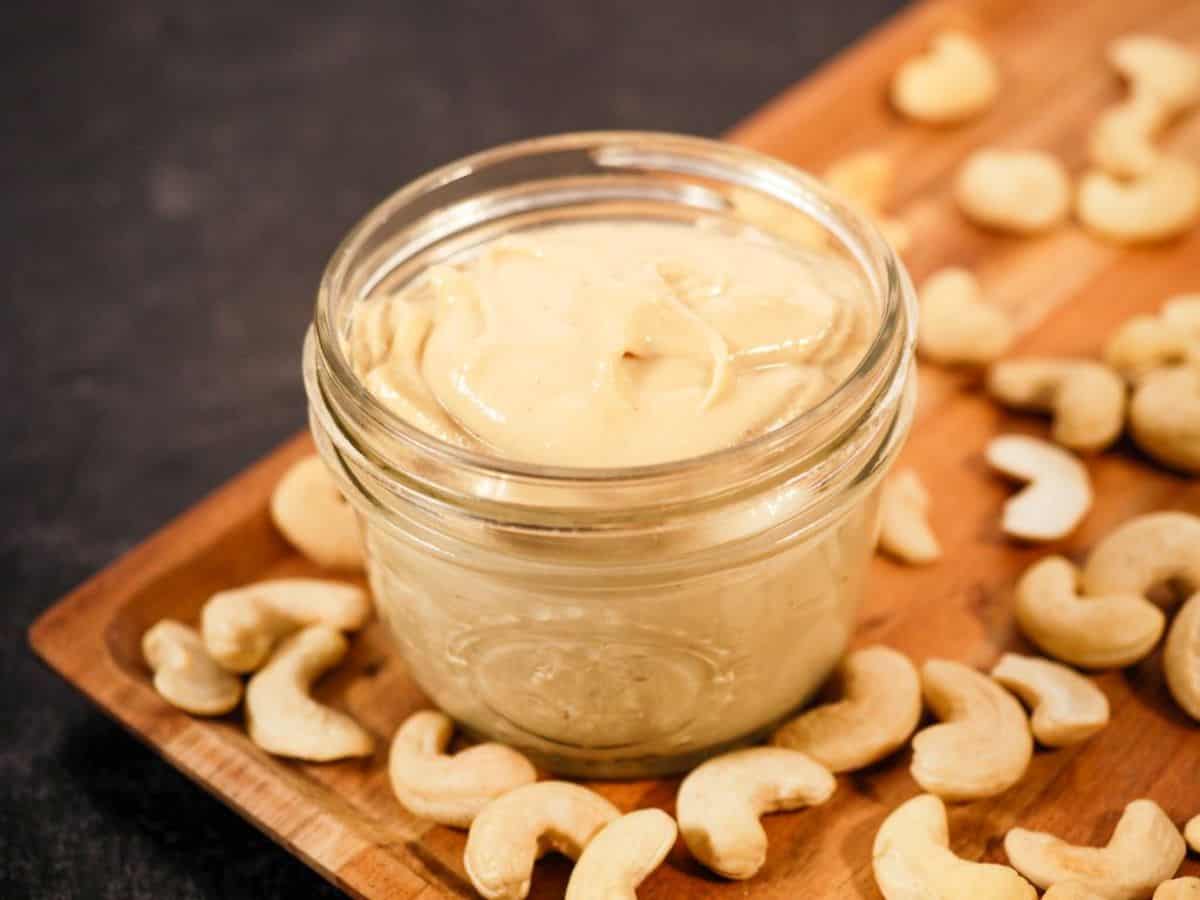 Cashew Butter in a glass jar on a wooden tray.