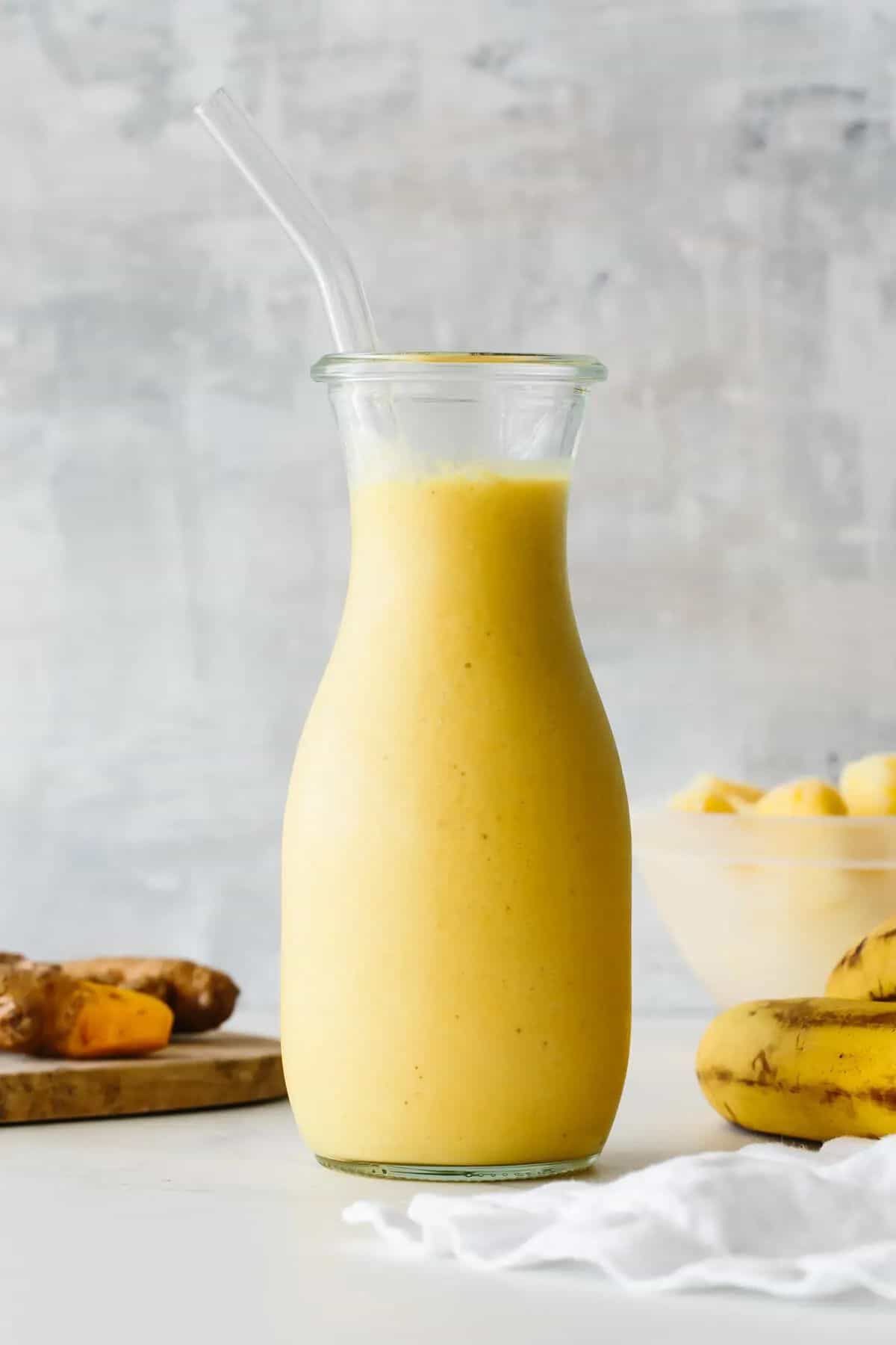 Turmeric Pineapple Smoothie in a glass bottle with a straw.